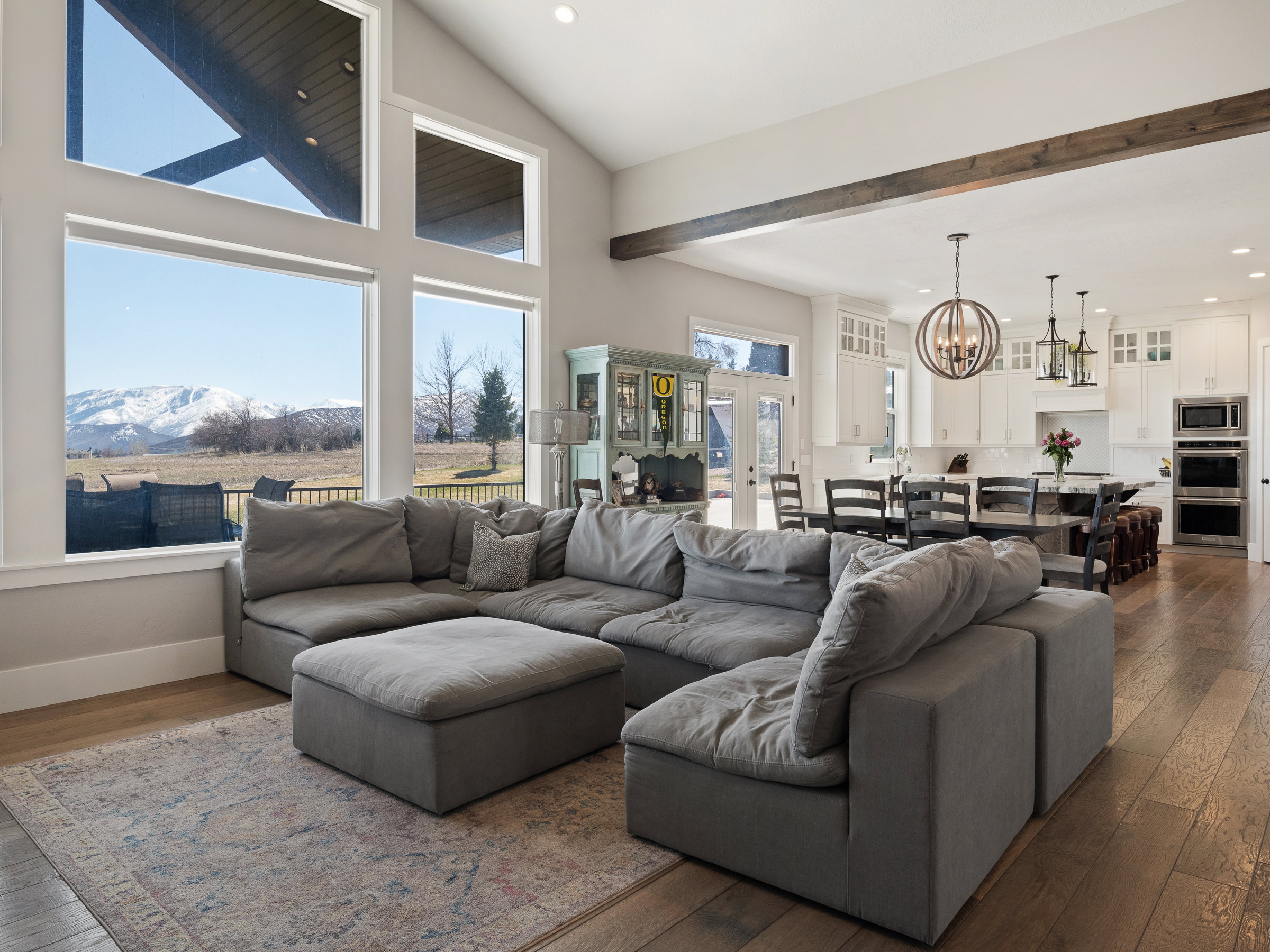 Expansive living area featuring a vaulted ceiling with exposed wood beams, large picture windows, and wood-finish flooring