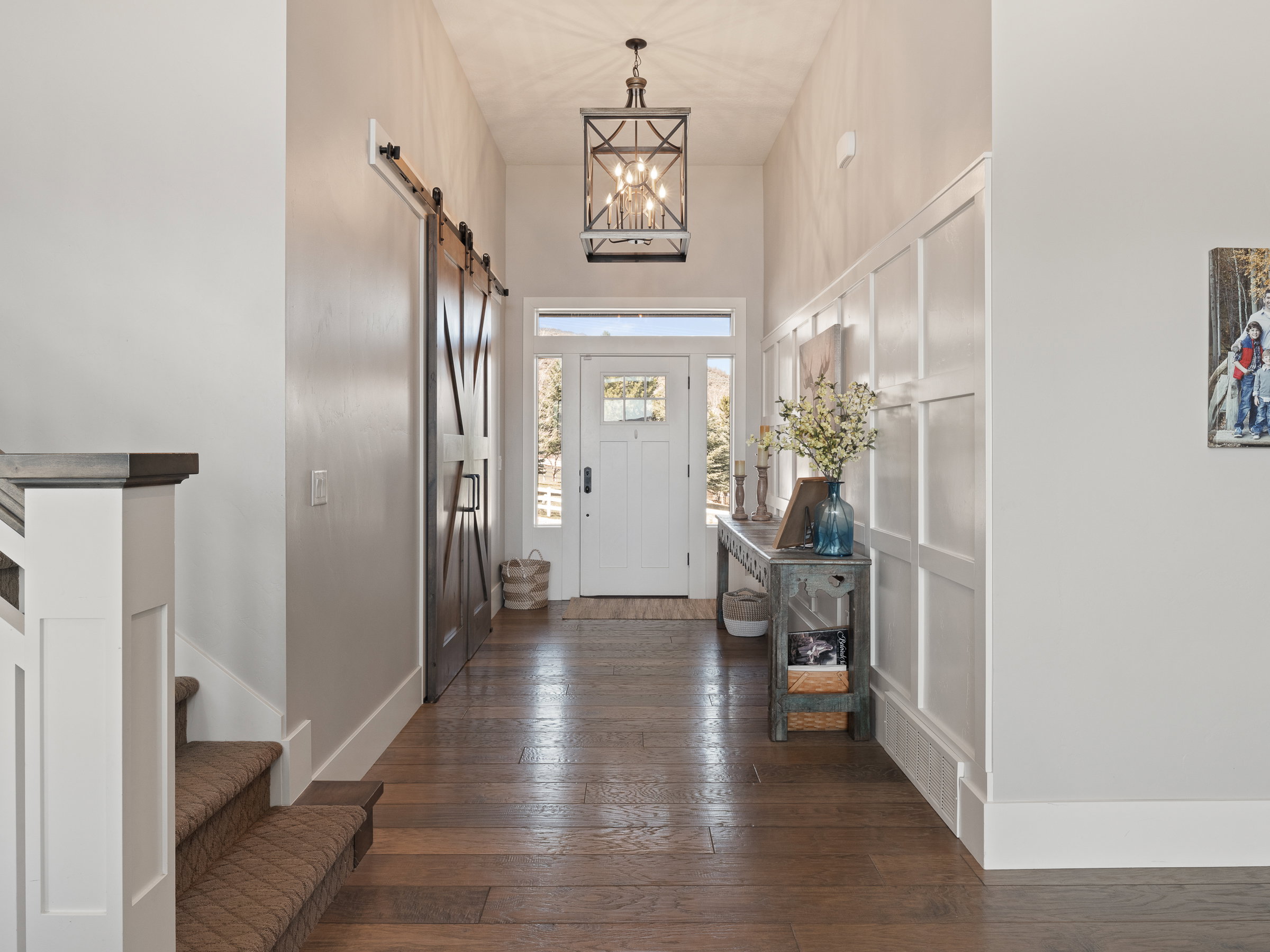 Foyer featuring wood-finish flooring, a white front door with sidelights, board and batten wall detailing, a dark bronze pendant light fixture, and a dark wood barn door