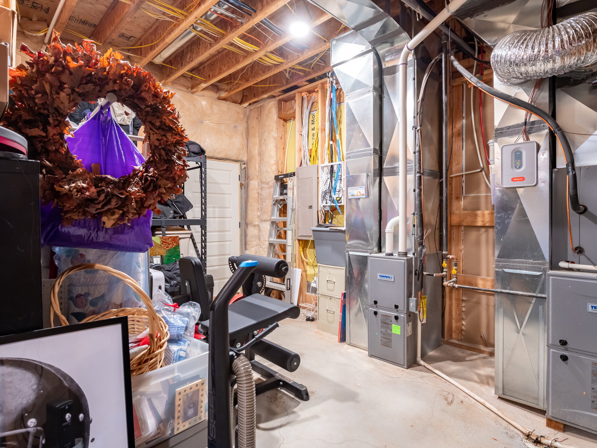 Basement mechanical room featuring exposed ductwork, a water heater, furnace units, and a concrete floor