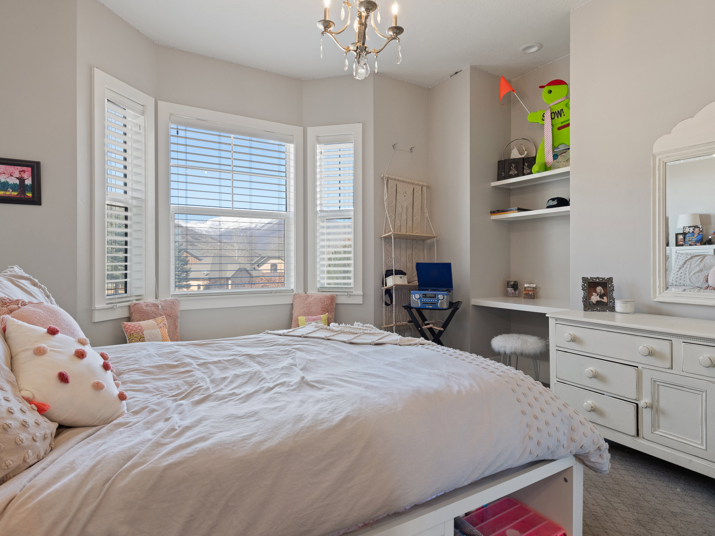 Room featuring a bay window, white plantation shutters, built-in shelving, and a built-in desk area