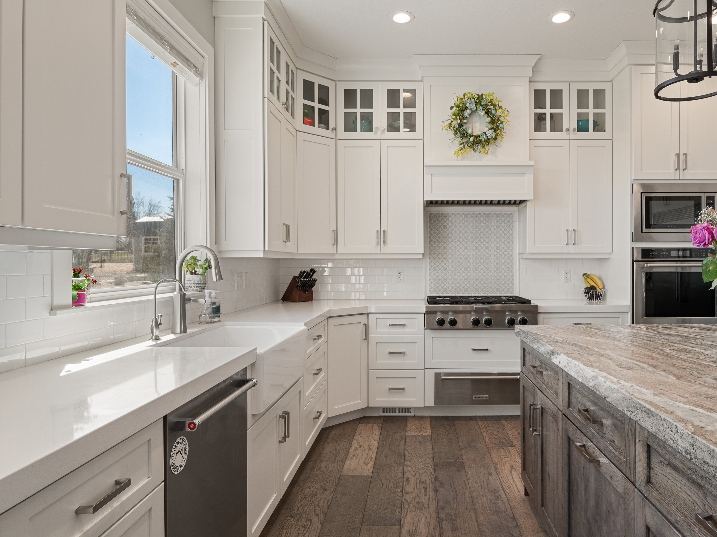 Gourmet kitchen featuring extensive white cabinetry, professional-grade range with custom hood, stainless steel appliances, a large window over the sink, and wood-finish flooring