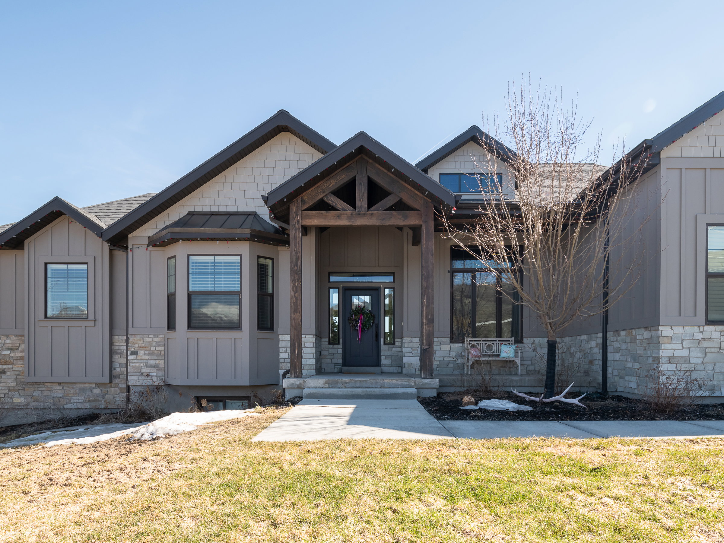 Craftsman-style exterior featuring a prominent timber-frame entry, board and batten siding, stone accents, dark-framed windows, and a bay window