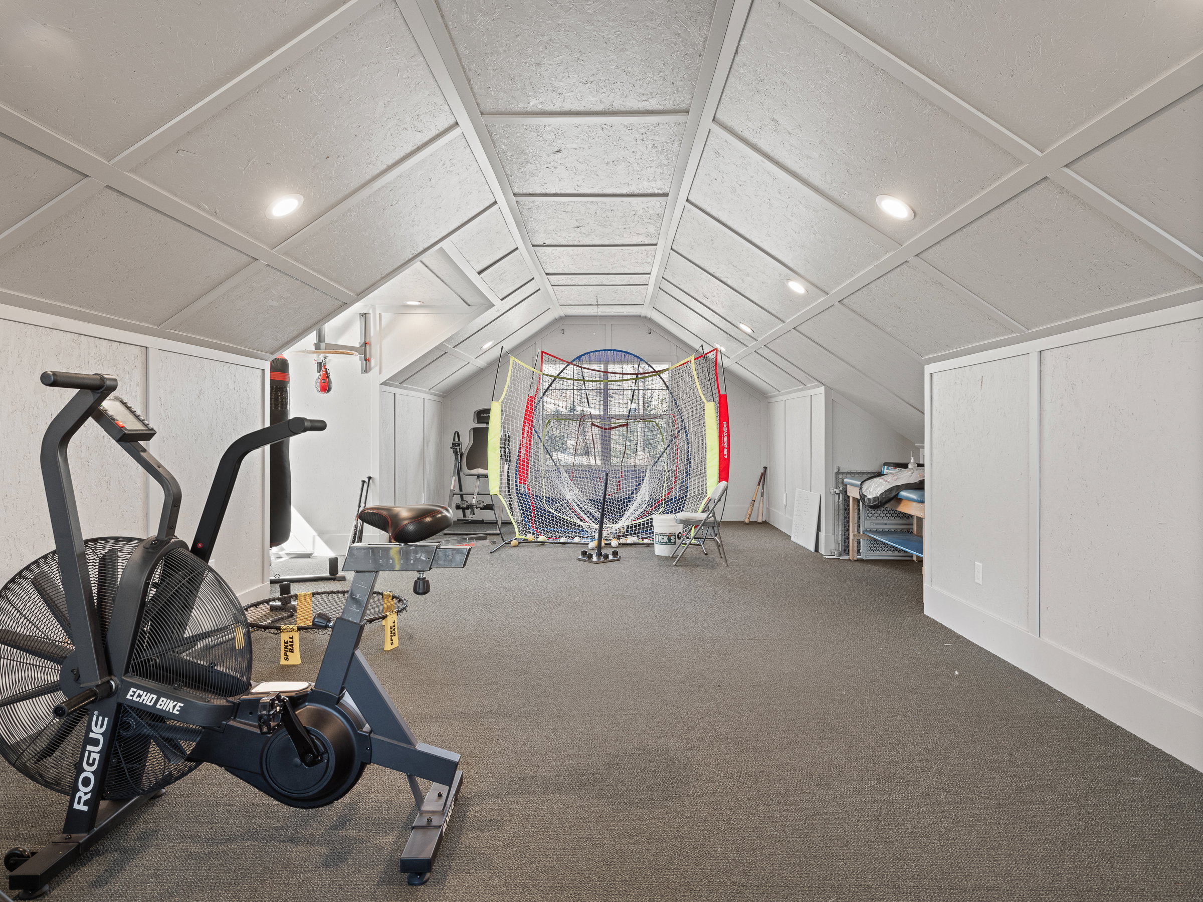 Spacious interior room featuring sloped ceilings with recessed lighting, textured wall panels, and dark carpeting