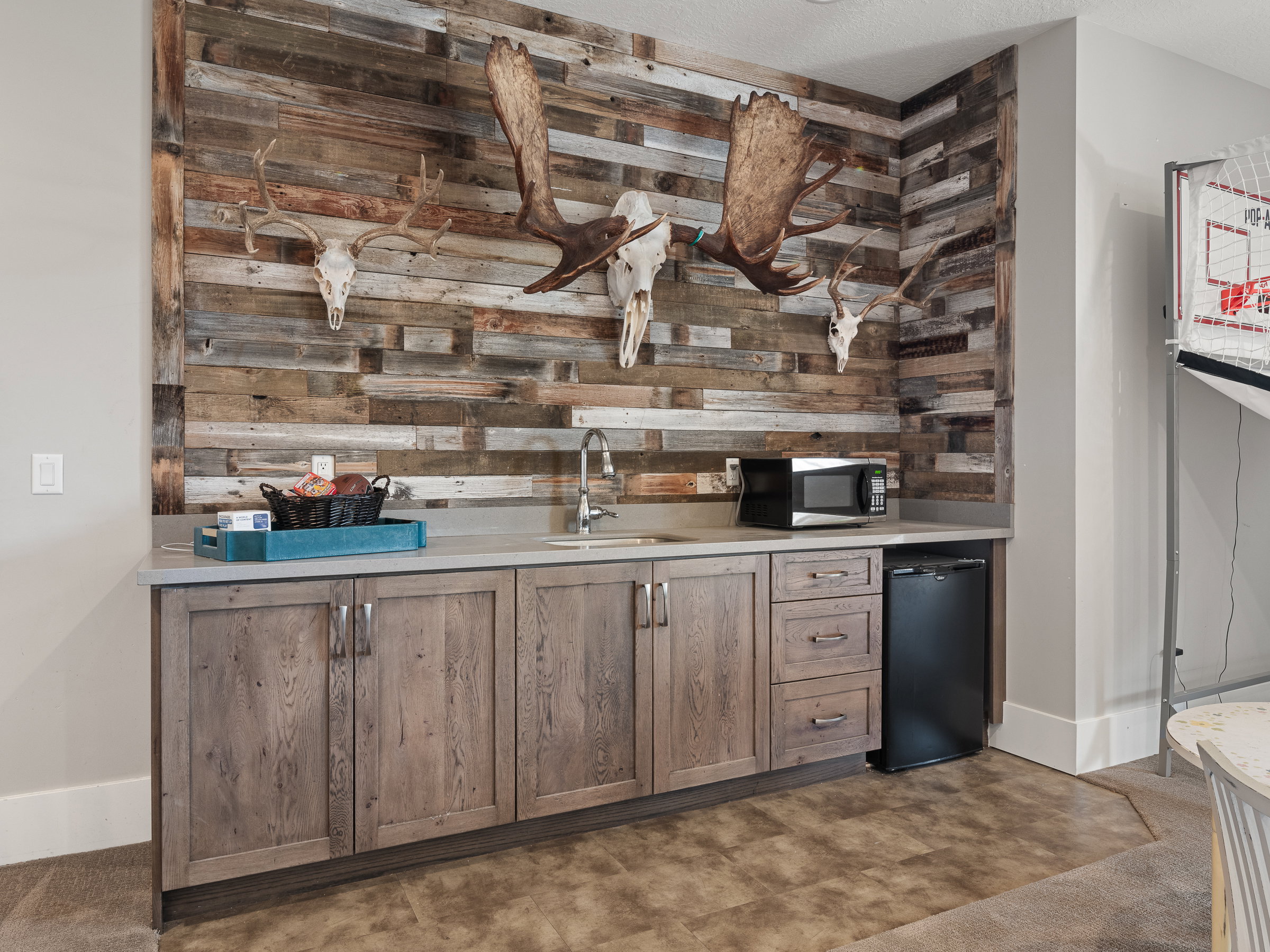 Custom wet bar featuring a paneled wood-finish accent wall, light grey countertops, a stainless steel sink with a gooseneck faucet, and integrated wood-finish cabinetry