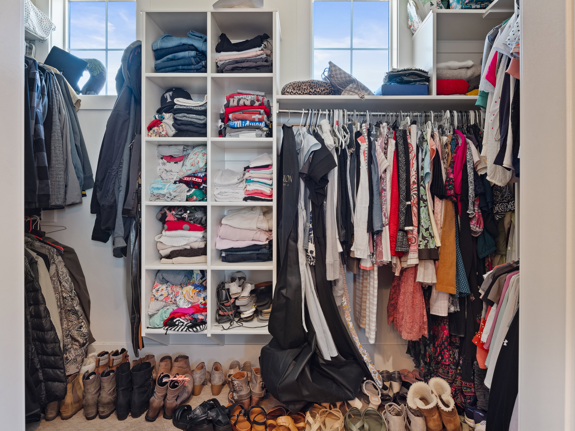 Built-in closet organization system featuring multiple shelving units, double hanging rods, and transom windows providing natural light