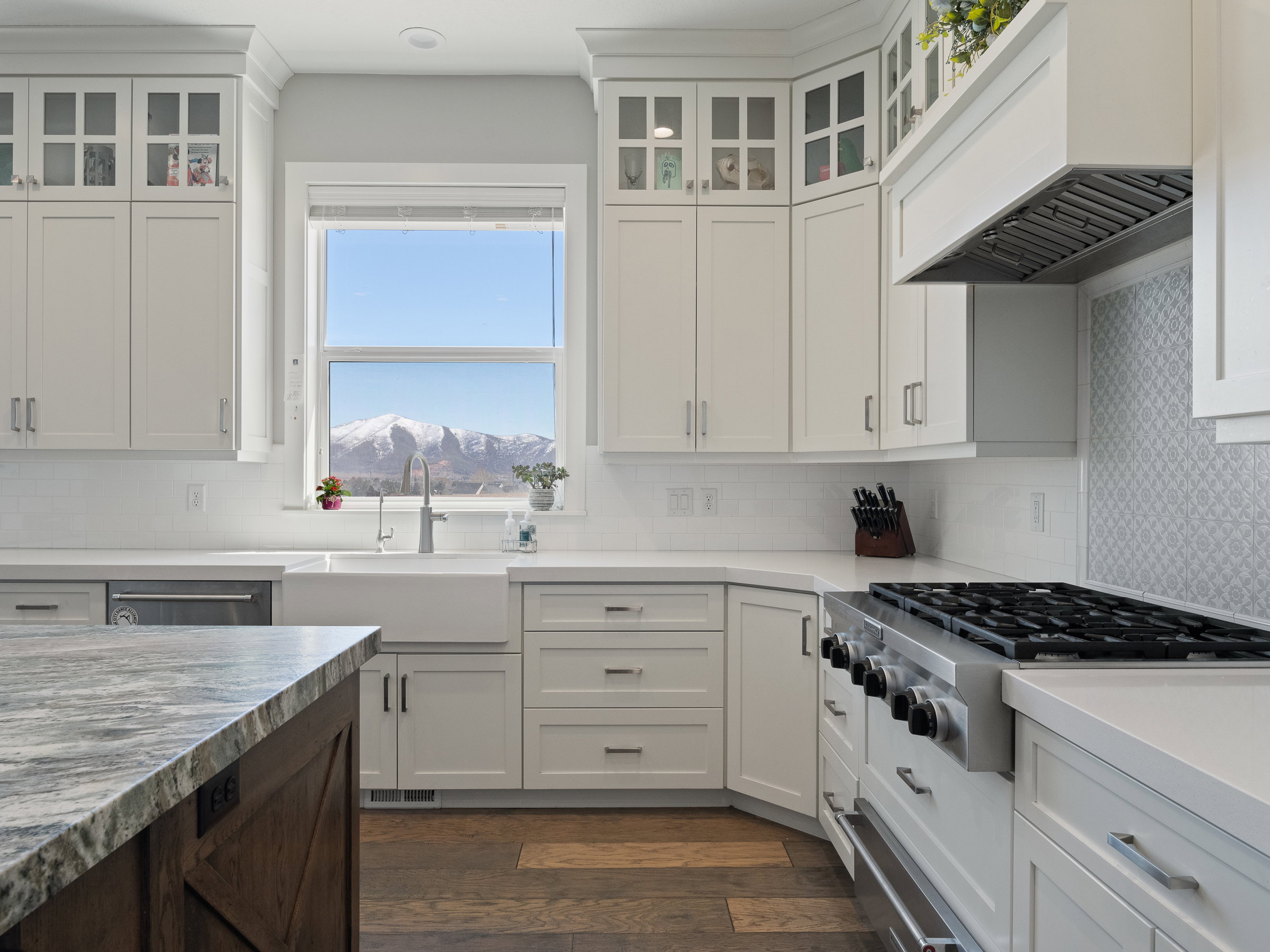 Spacious kitchen featuring white shaker cabinetry, an apron-front sink, a professional-grade range, quartz countertops, and wood-finish flooring