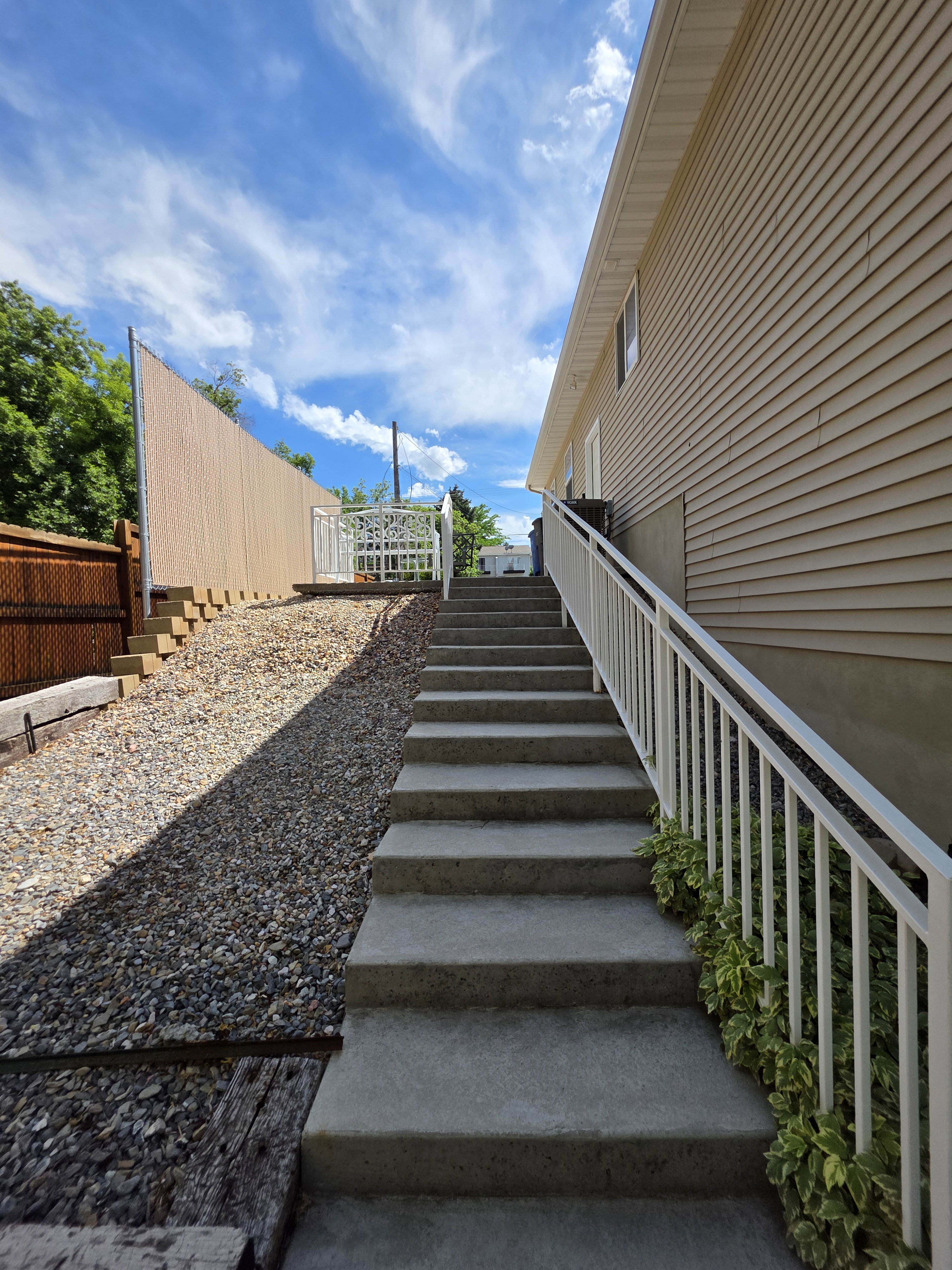 Exterior stairs with white railings lead to an upper landing, flanked by gravel landscaping and a privacy fence