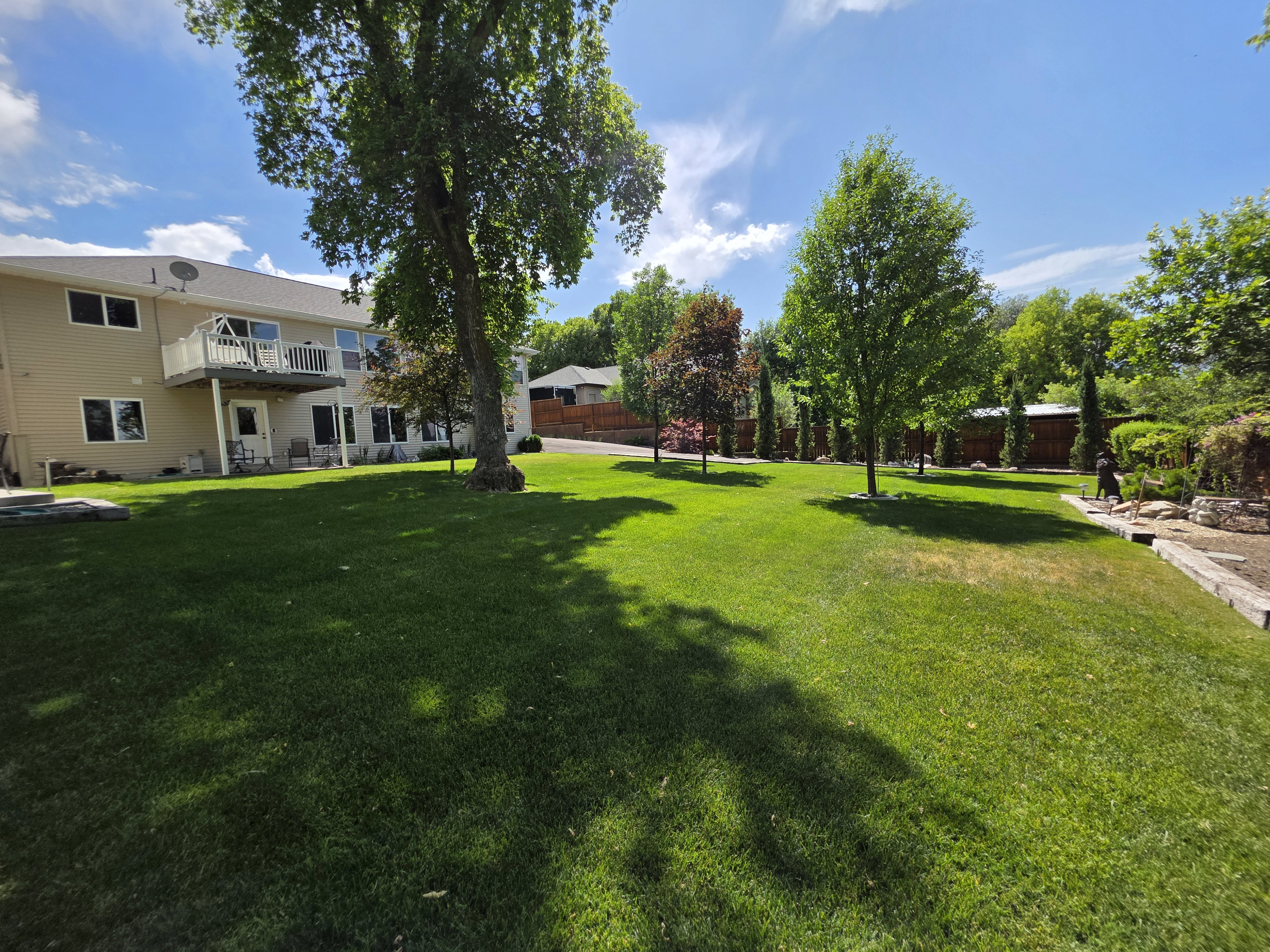 Expansive lawn with mature trees, a multi-story exterior, and a second-level deck with white railing