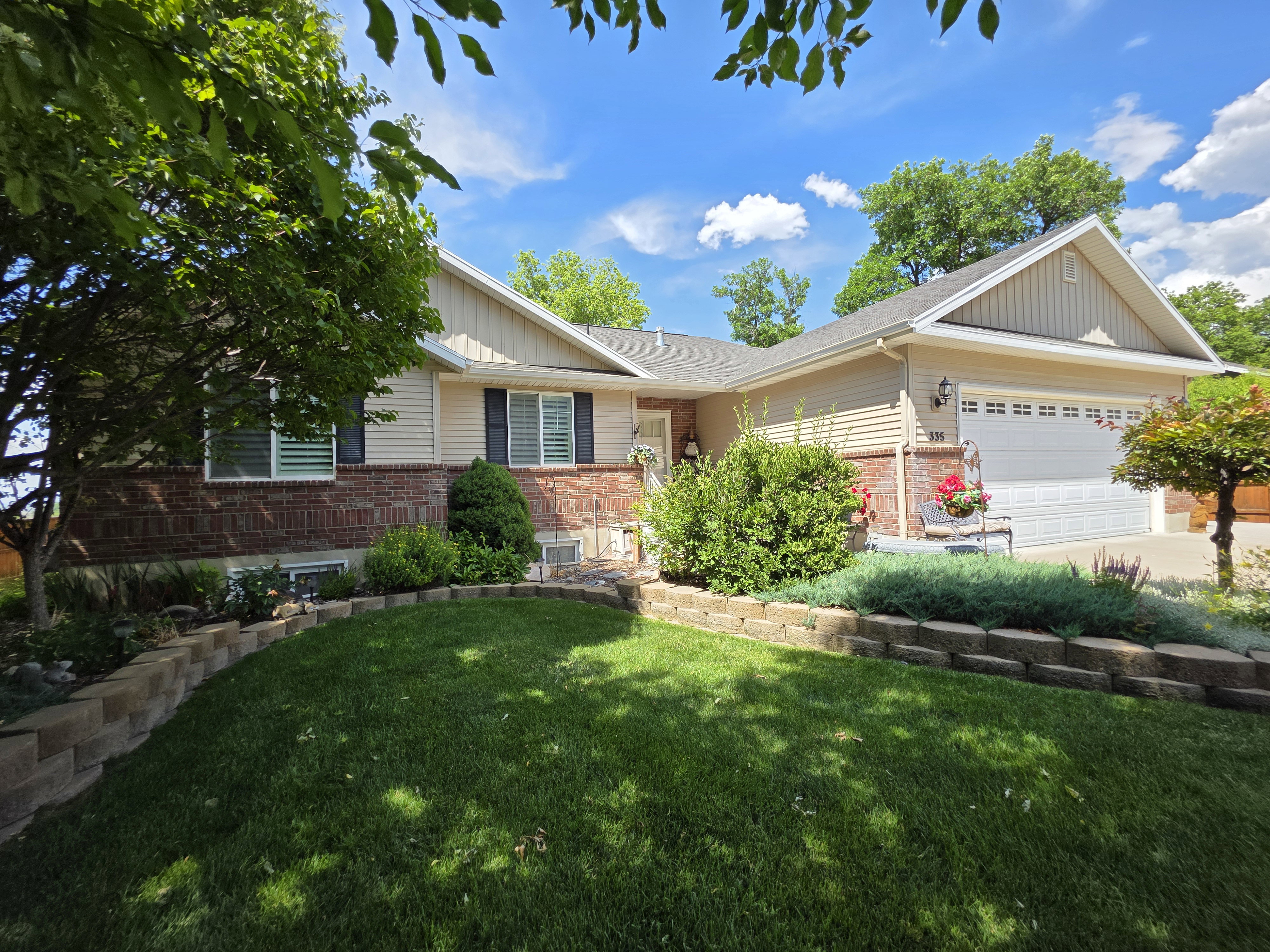 Residential exterior with a brick and siding facade, featuring a manicured front lawn and mature trees