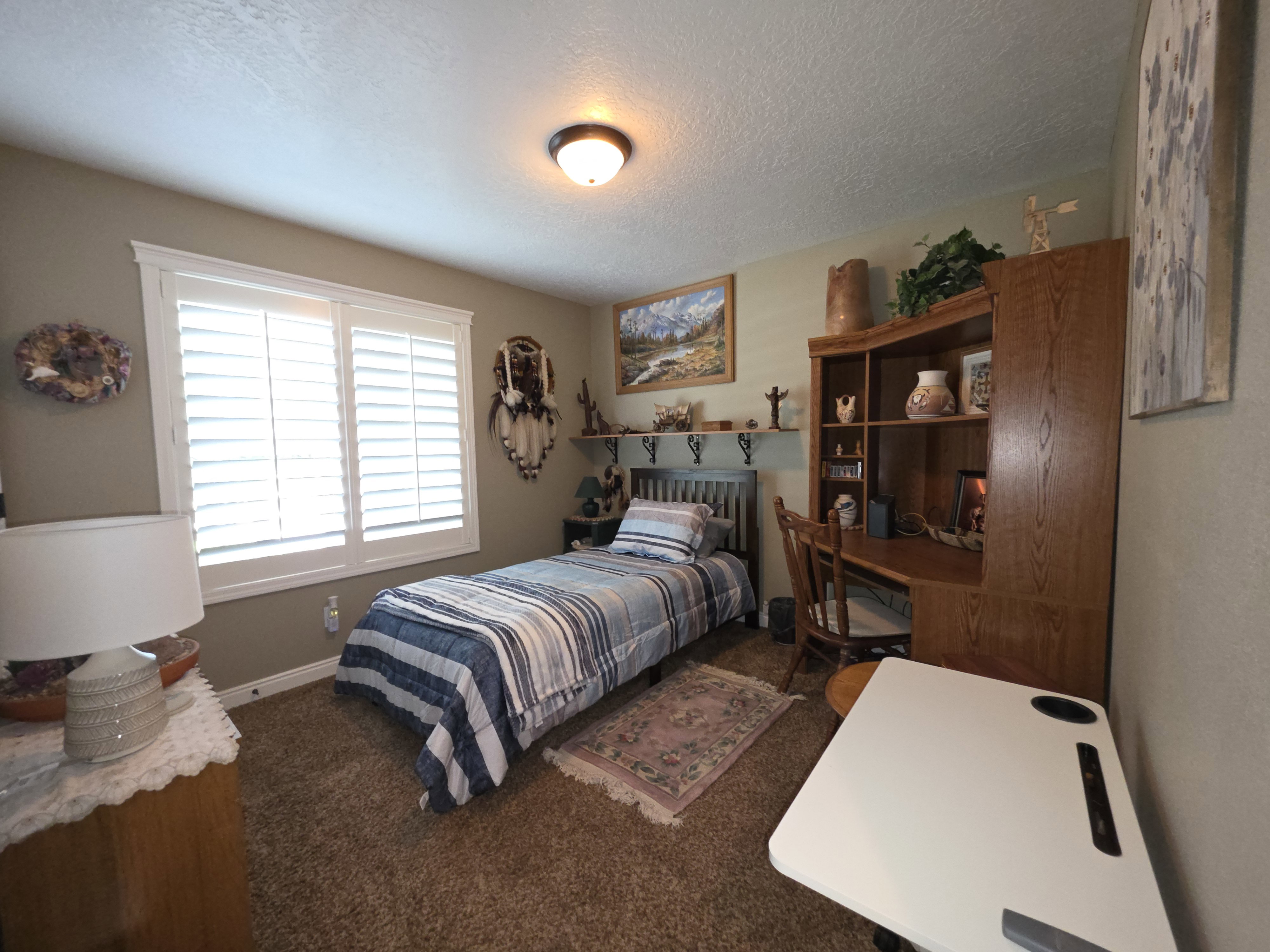 Carpeted room featuring a window with white plantation shutters, built-in shelving, and a desk area