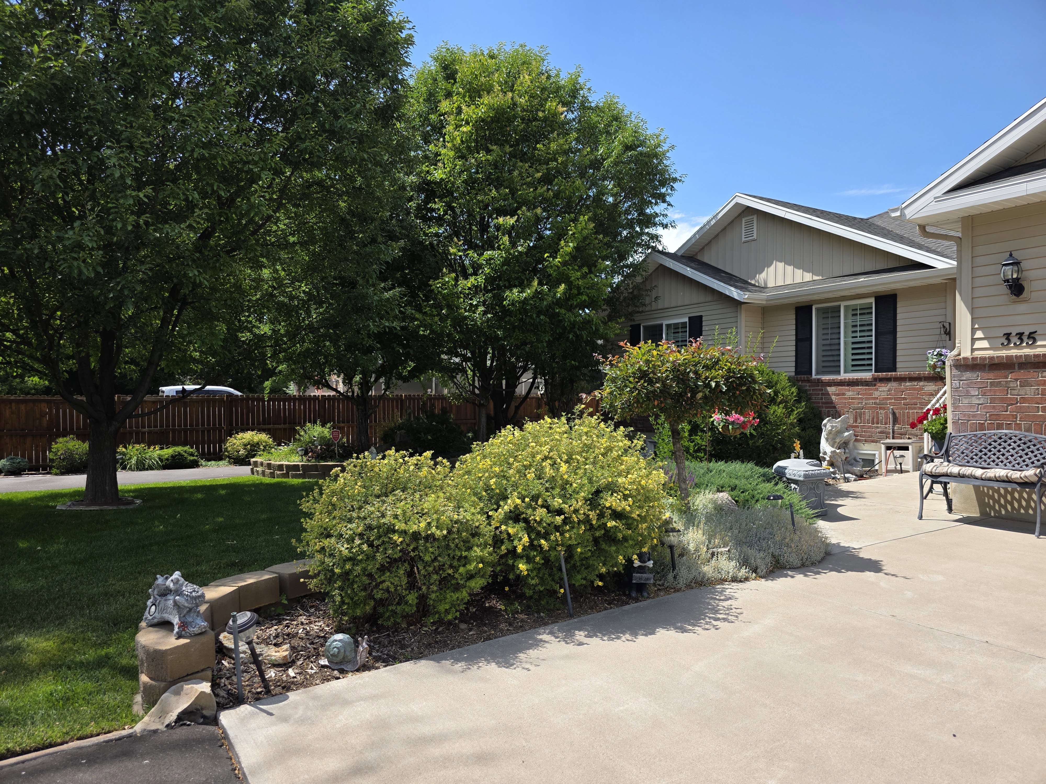 Manicured front yard with mature trees, established landscaping, concrete driveway, and brick accent siding