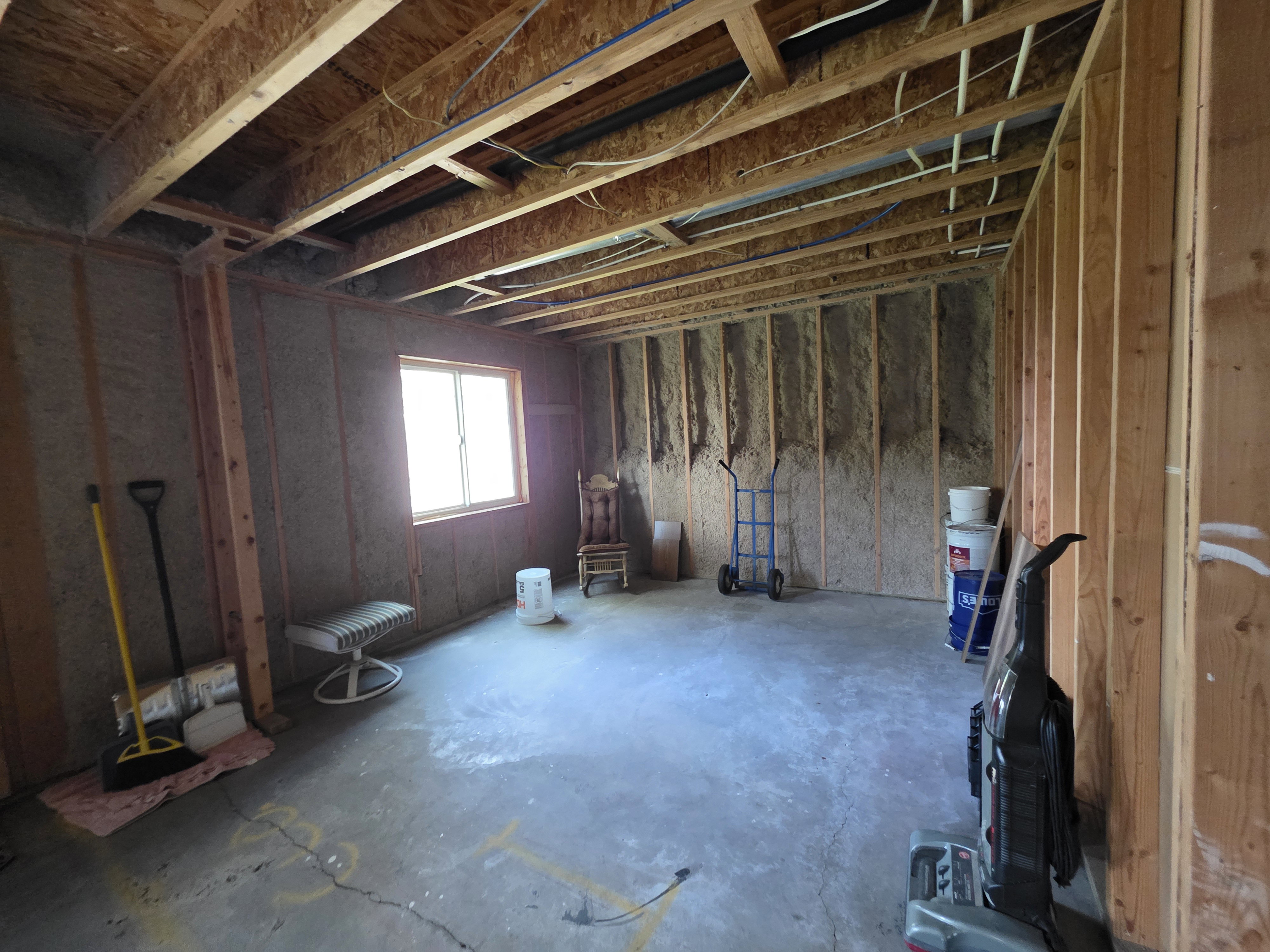 Unfinished interior space featuring exposed wood framing, concrete flooring, a single window, and visible ceiling joists