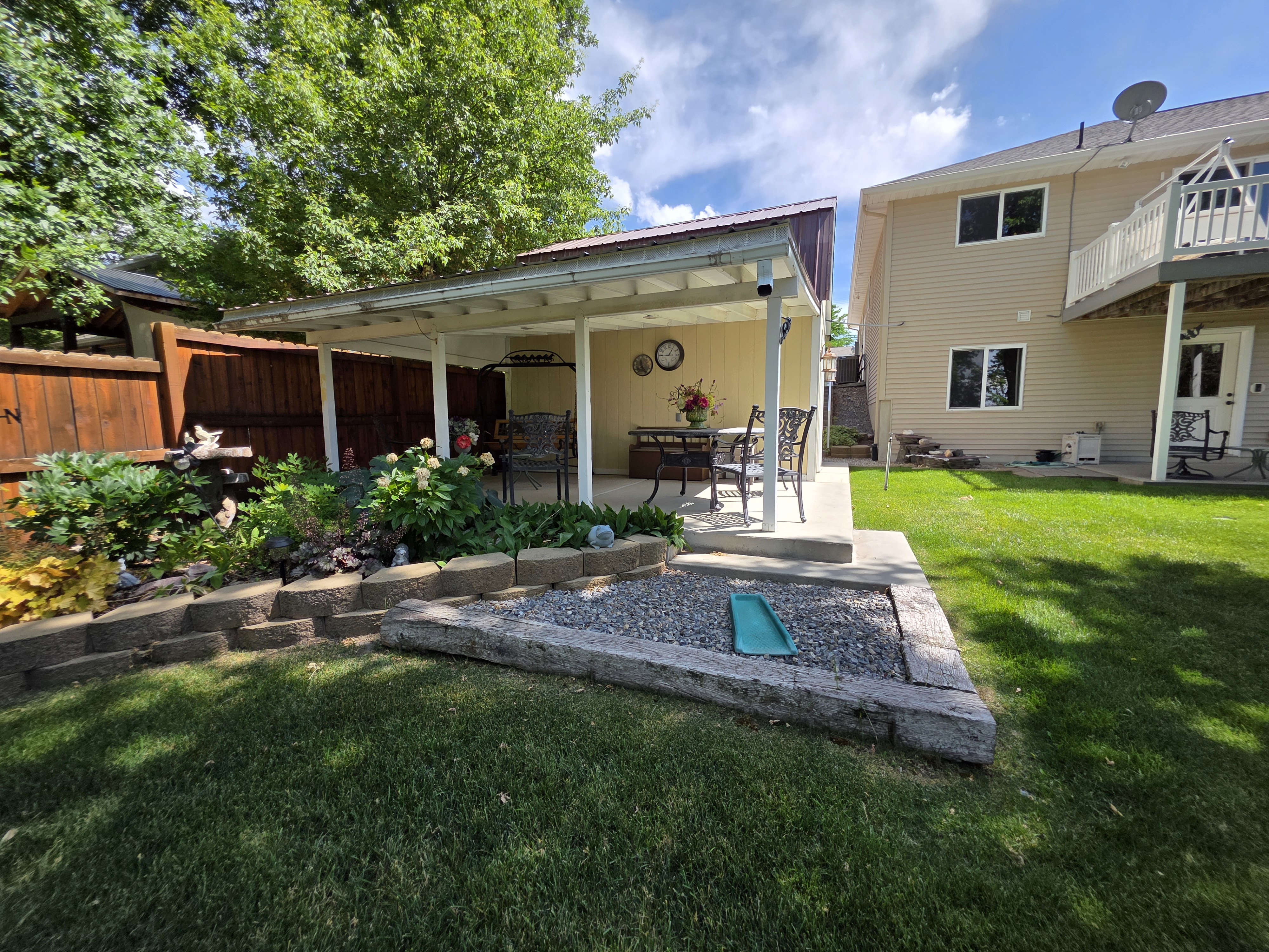 Covered patio with a concrete surface, featuring a tiered retaining wall, a dedicated gravel area, and established plantings