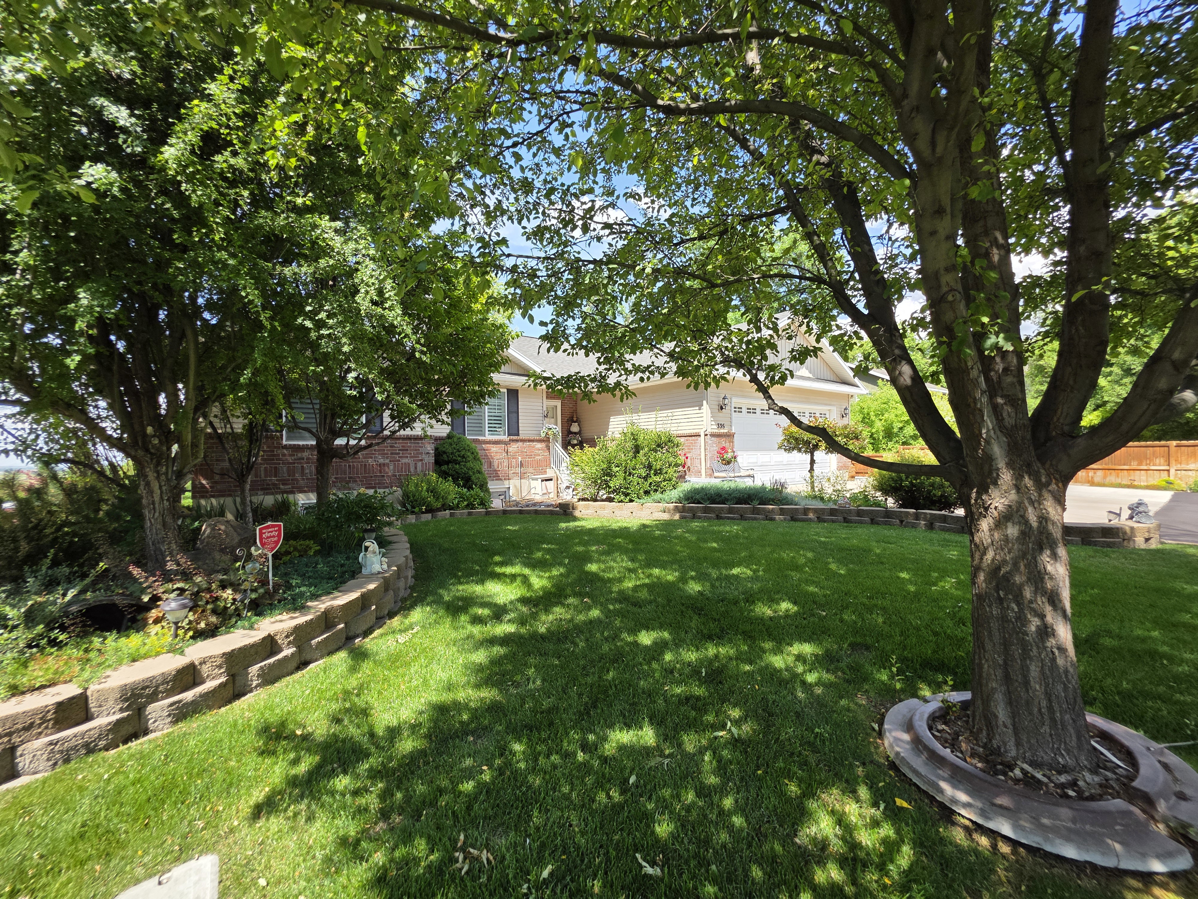 Front exterior featuring mature trees, a manicured lawn, a retaining wall, and a two-car garage
