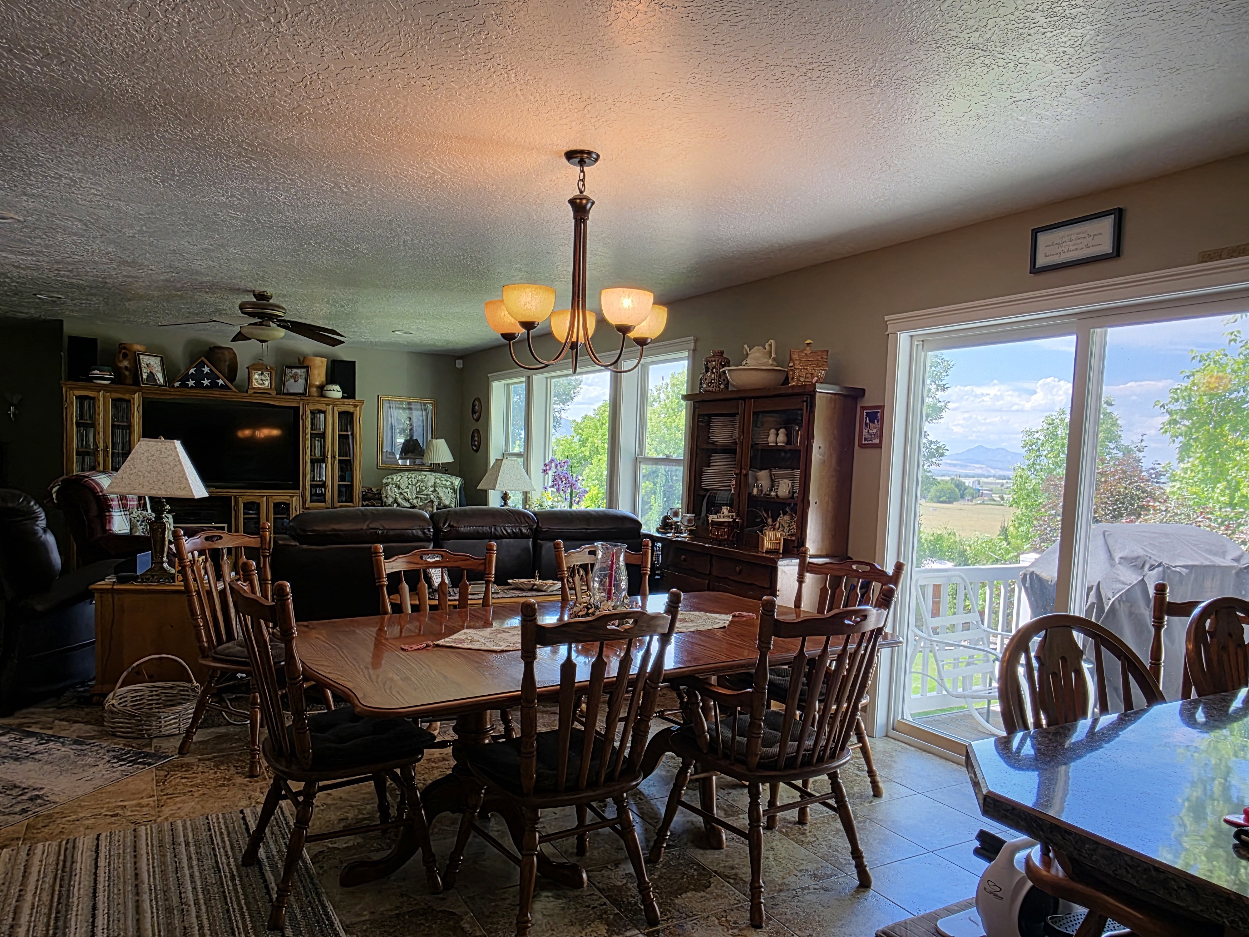 Open-concept living and dining area featuring a wood-finish dining table with matching chairs, an overhead chandelier with amber-toned shades, and a ceiling fan