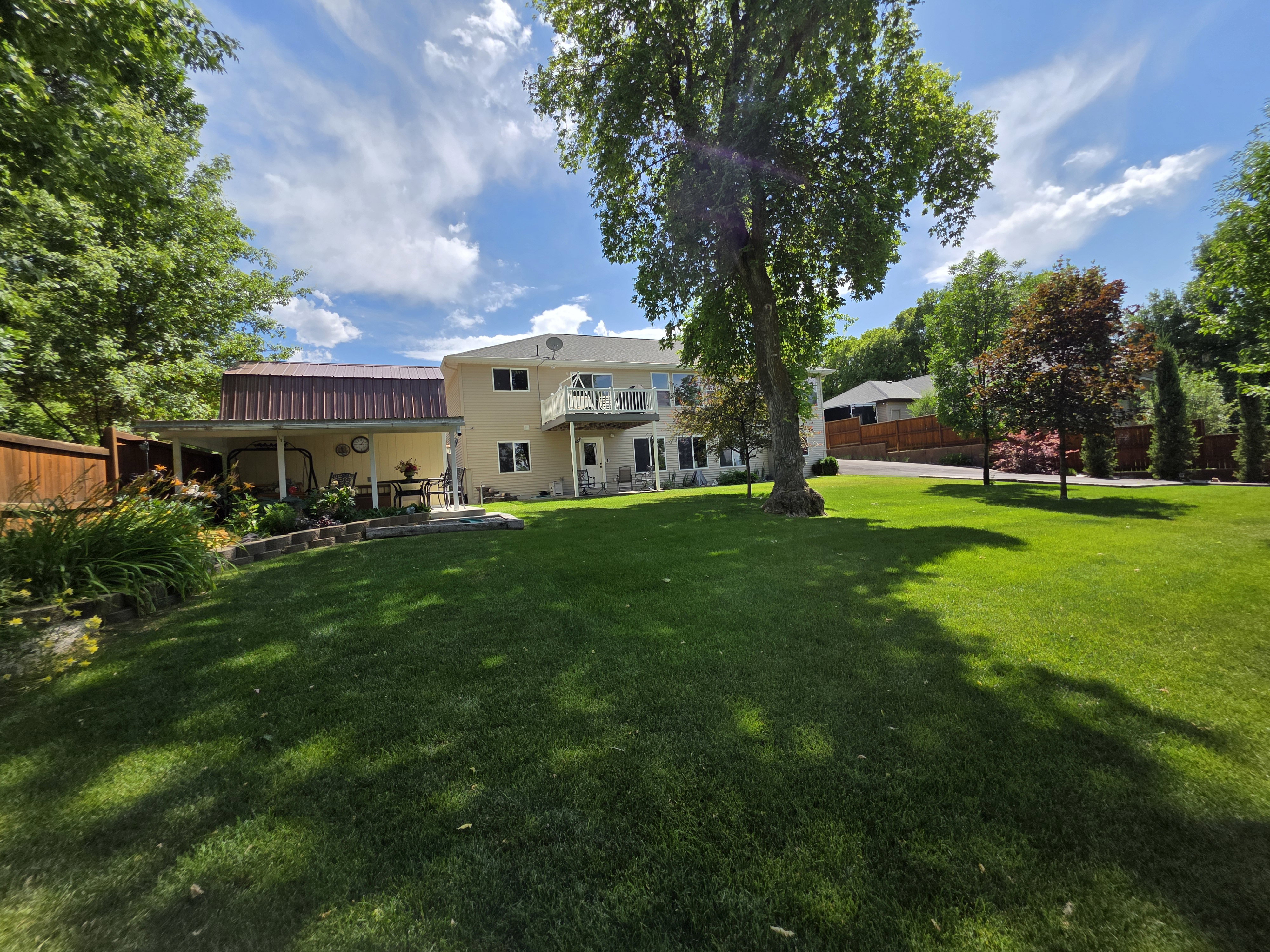 Expansive backyard with a manicured lawn, mature trees, and a covered patio featuring a metal roof