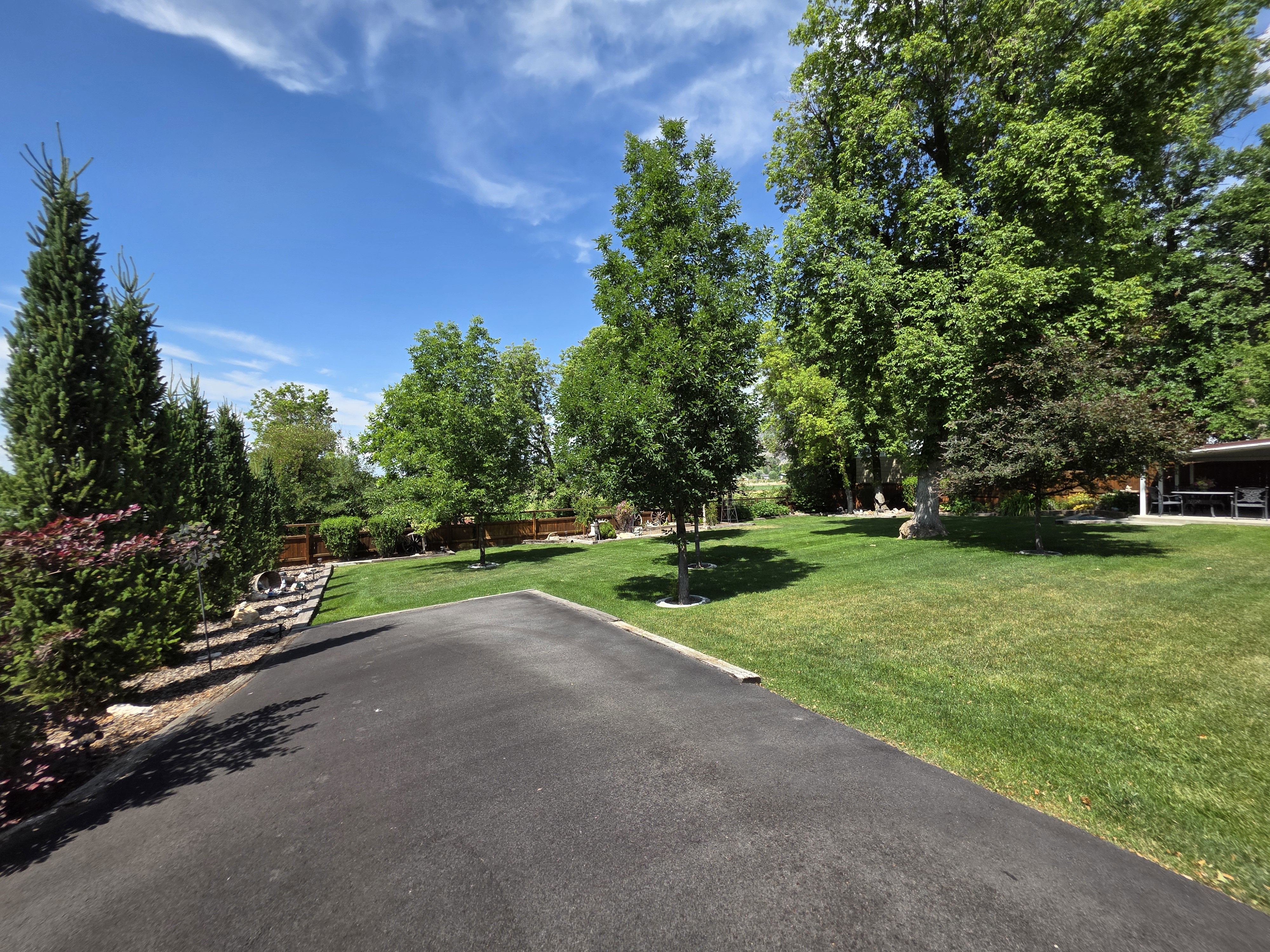 Asphalt driveway bordered by manicured lawn and mature trees