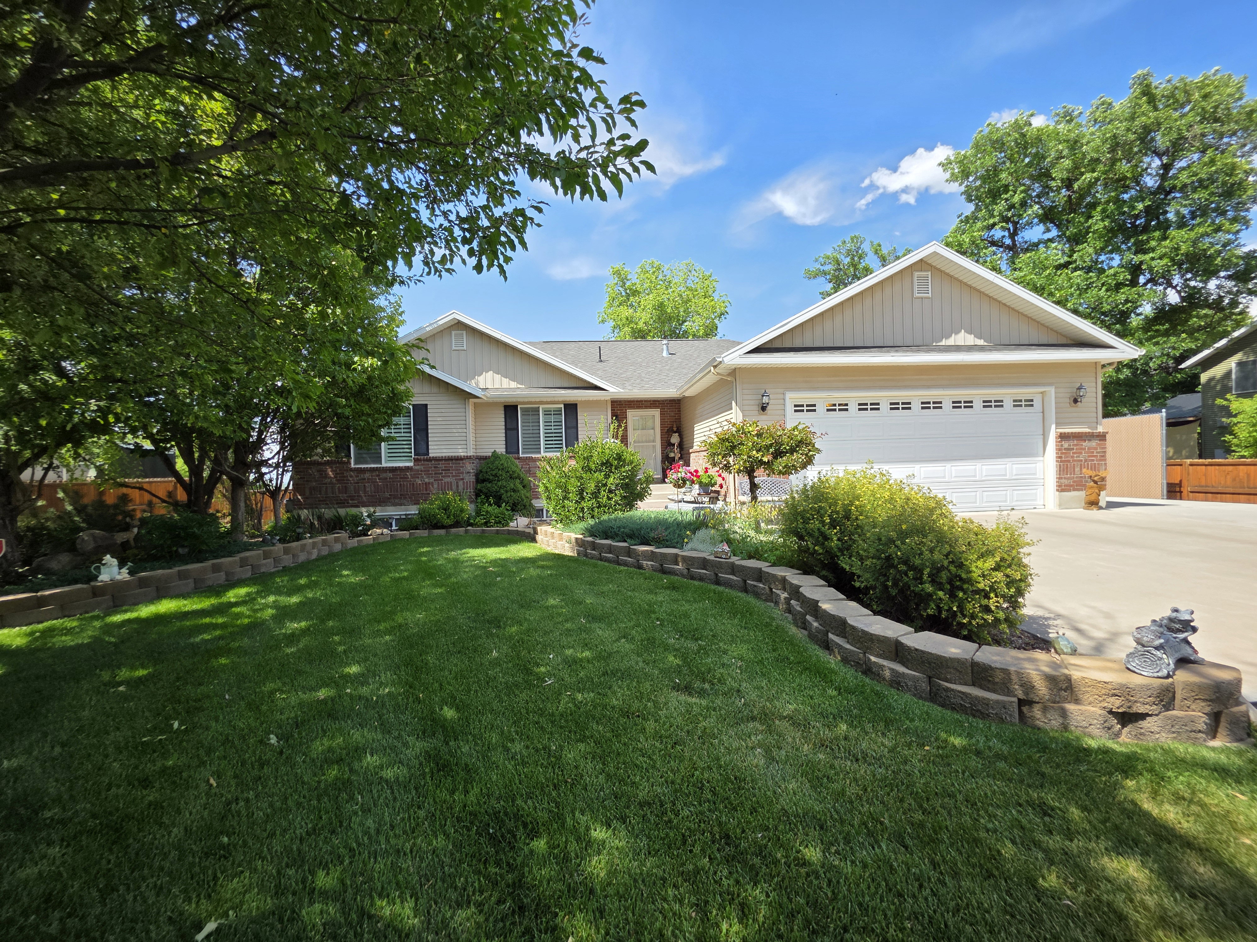 Front exterior featuring a two-car garage, brick accents, and a sloped lawn with retaining walls