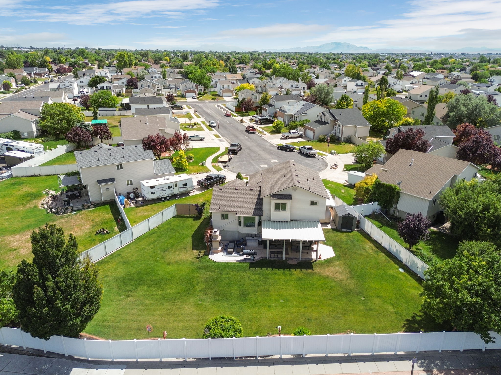 Spacious backyard featuring a manicured lawn, white privacy fencing, and a covered patio