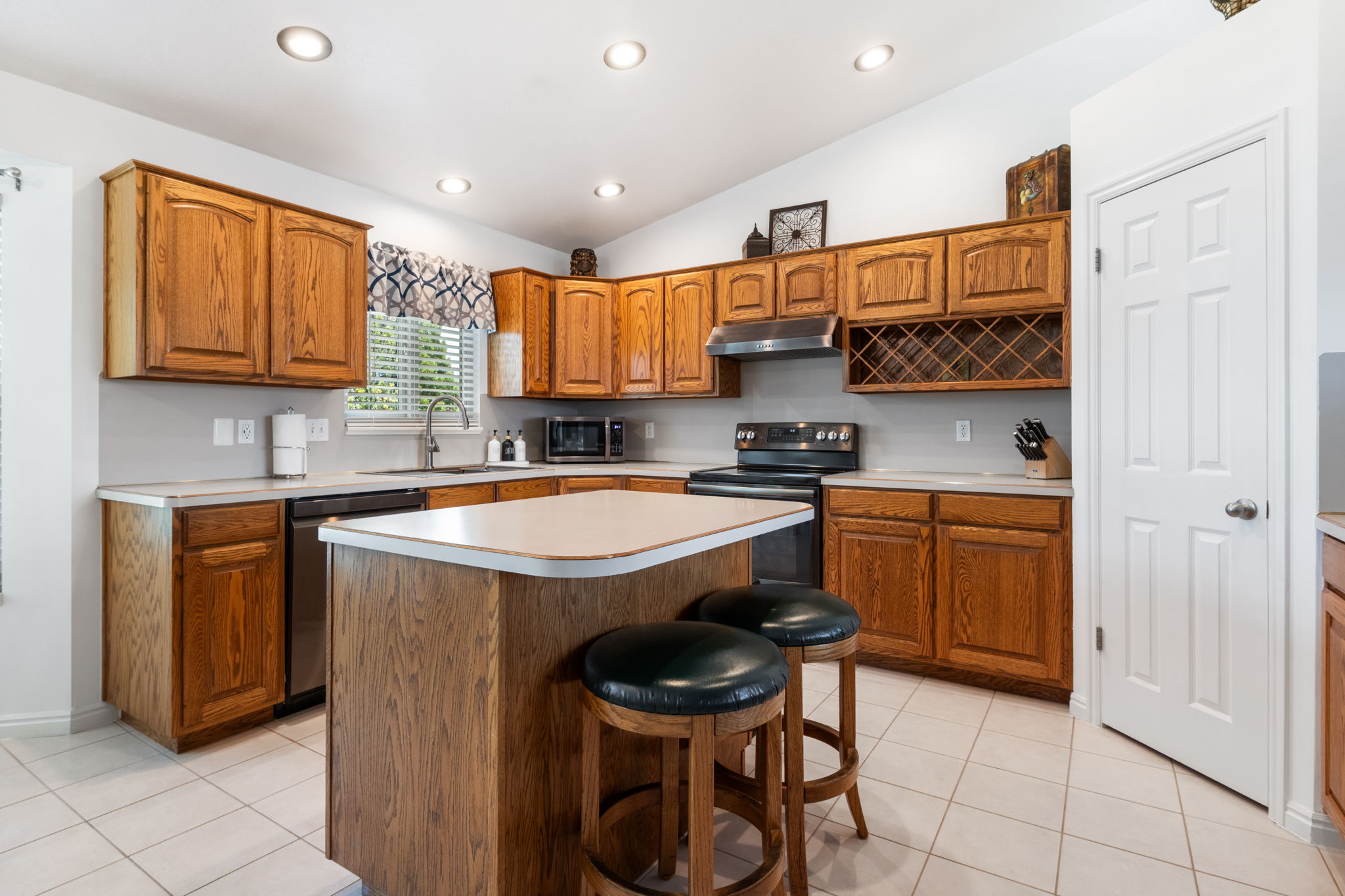 Kitchen featuring recessed lighting, a central island with countertop, extensive wood cabinetry, white tile flooring, and stainless steel appliances