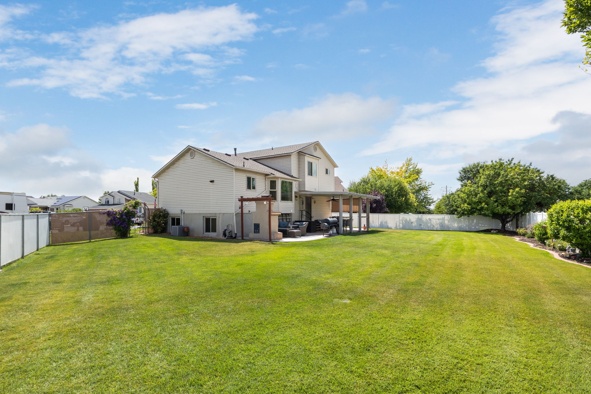 Expansive rear yard featuring a large green lawn, covered patio, and mature perimeter trees