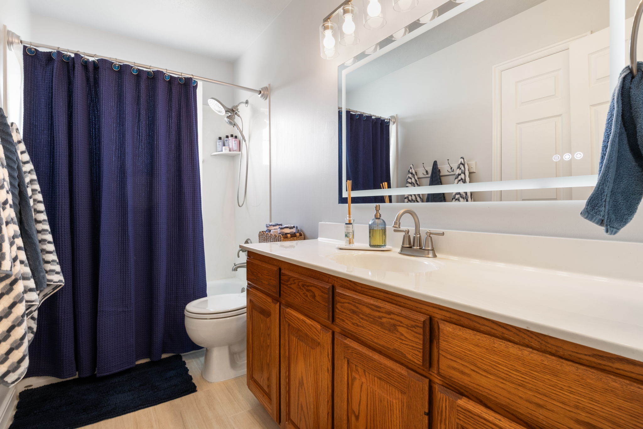 Bathroom featuring a wood-finish vanity with a white countertop, large wall-mounted mirror, and a bathtub with an overhead shower fixture