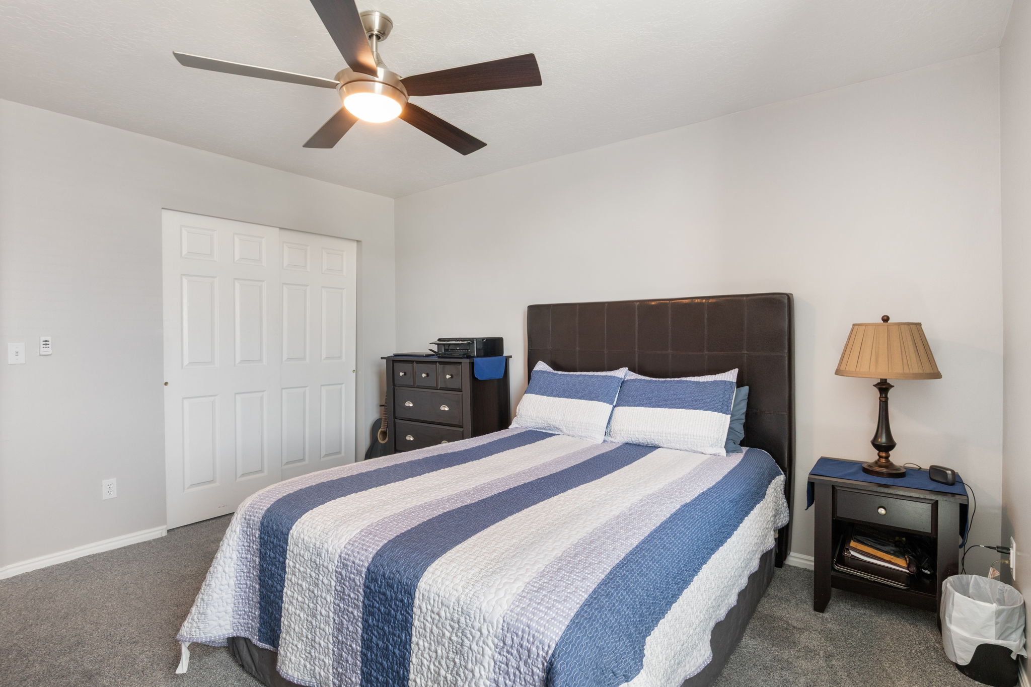 Bedroom featuring light gray walls, gray carpet flooring, a ceiling fan with integrated lighting, and a white bi-fold closet door