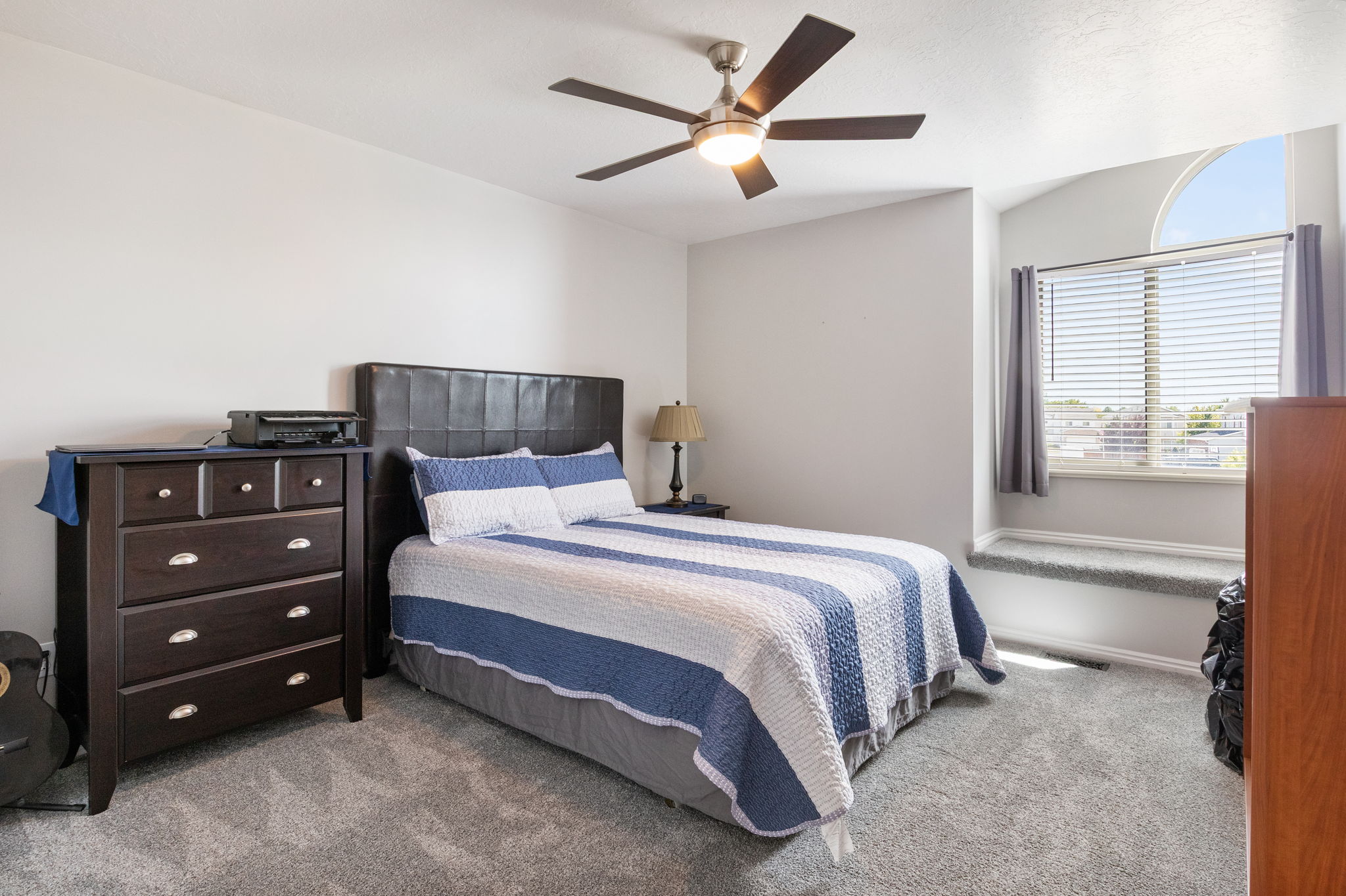 Carpeted room featuring a ceiling fan with integrated lighting, a large window with blinds, and a built-in window seat below