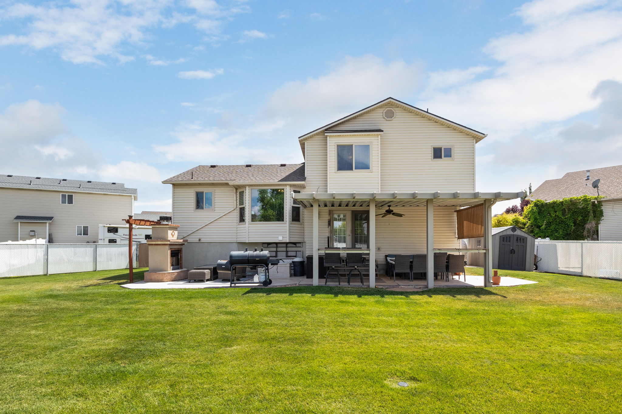 Expansive backyard featuring a manicured lawn, a large patio with a pergola, an outdoor fireplace, a built-in outdoor cooking station, and a storage shed