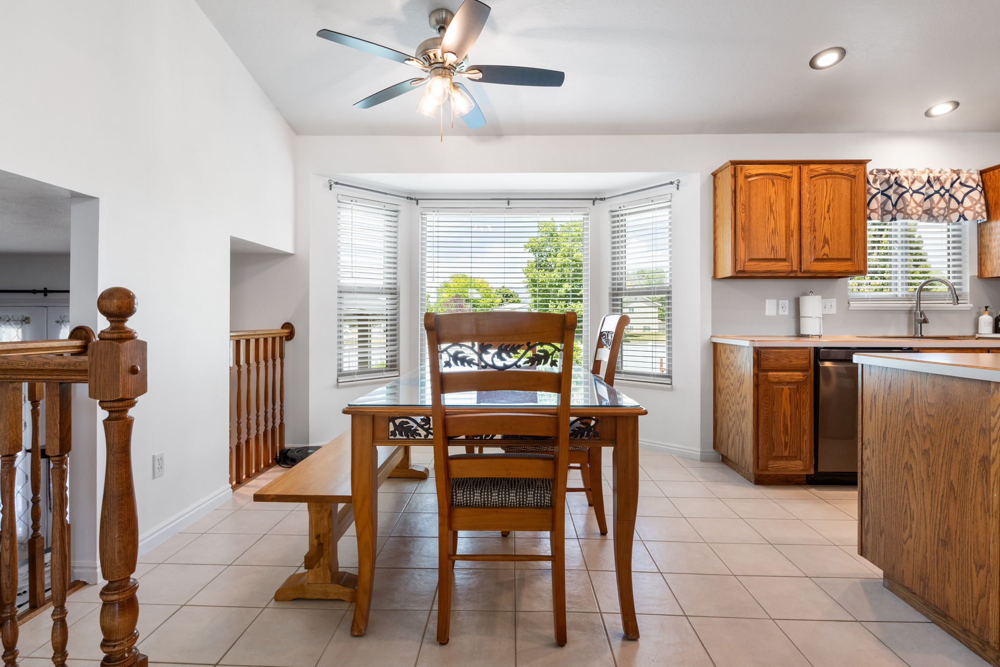 Kitchen and dining area featuring wood-finish cabinetry, a bay window with blinds, tile flooring, and recessed lighting