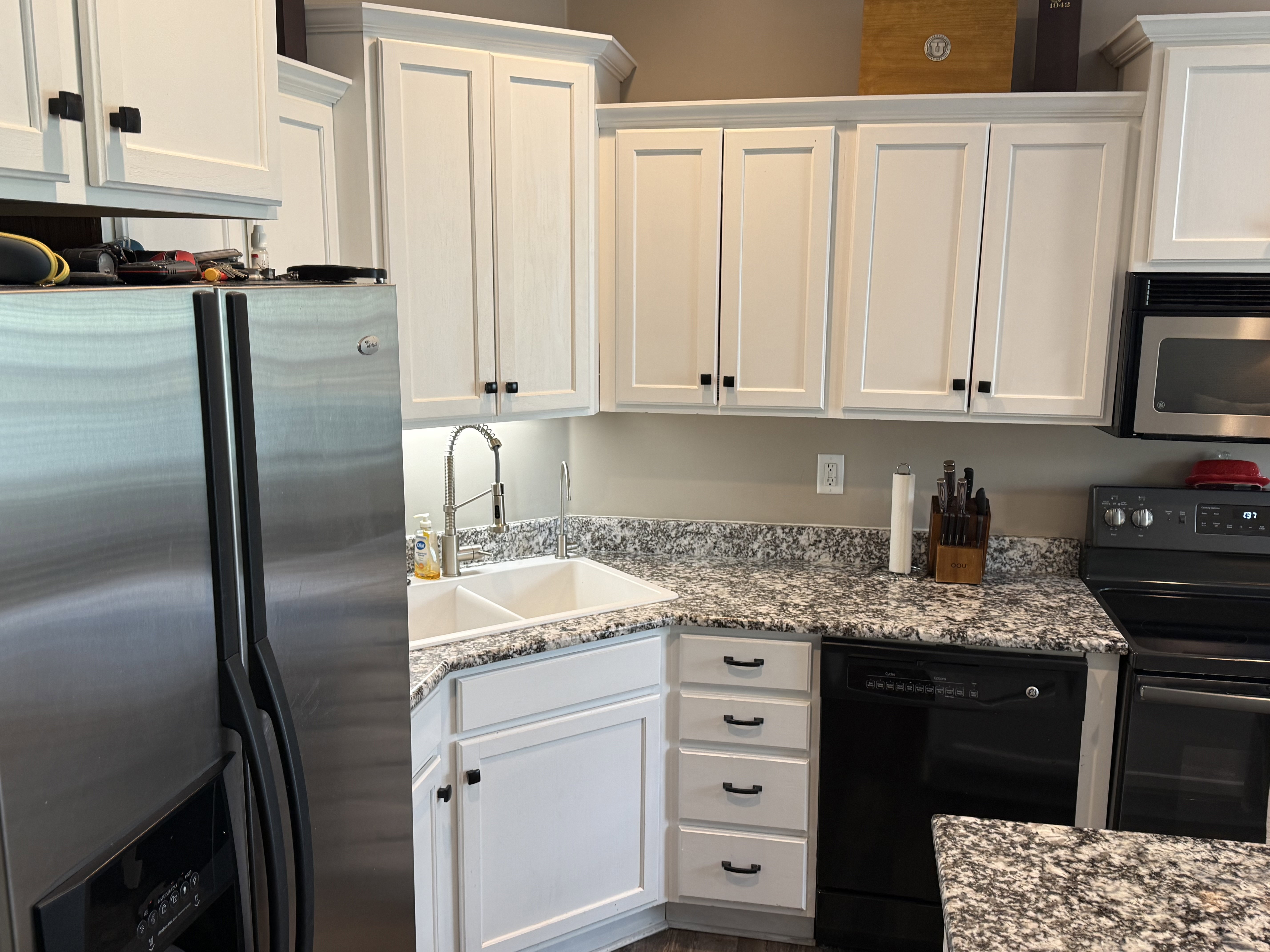 Kitchen featuring white shaker-style cabinetry, a double basin sink, stainless steel refrigerator, black dishwasher, and granite-style countertops