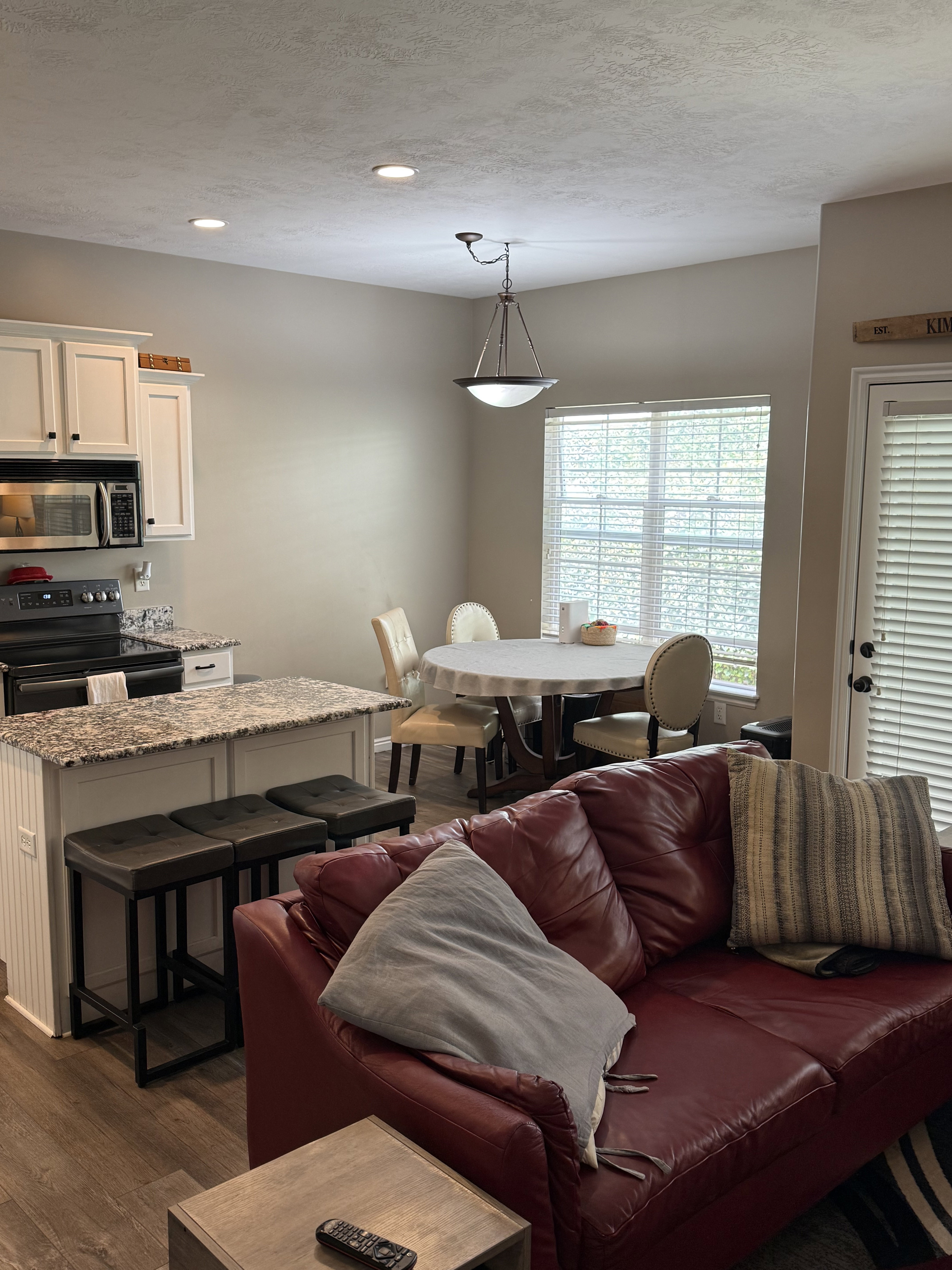 Integrated kitchen and dining area featuring white cabinetry, granite-style countertops, stainless steel microwave, and wood-finish flooring