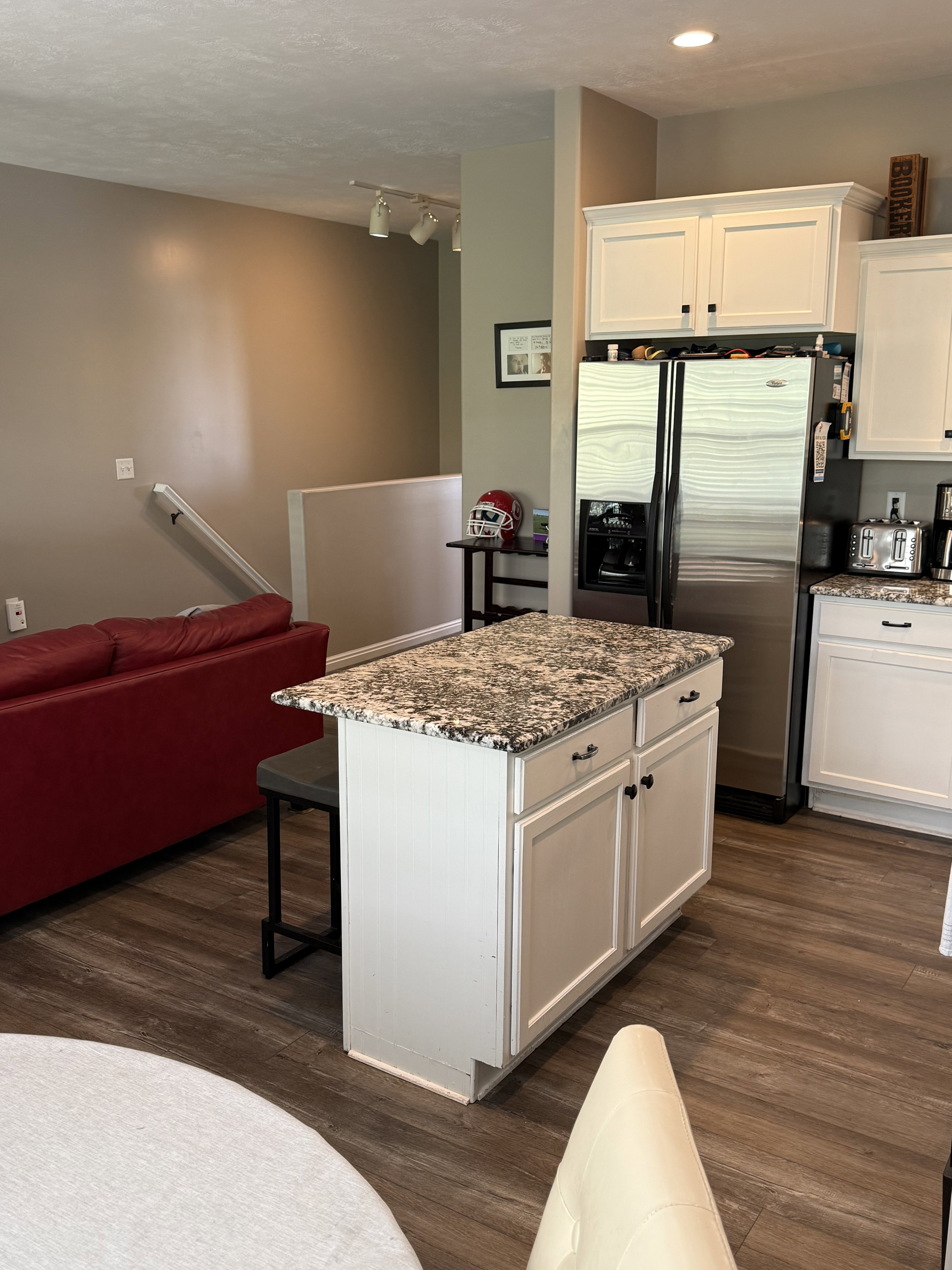 Kitchen island featuring a stone-finish countertop, white cabinetry with dark hardware, and wood-finish flooring