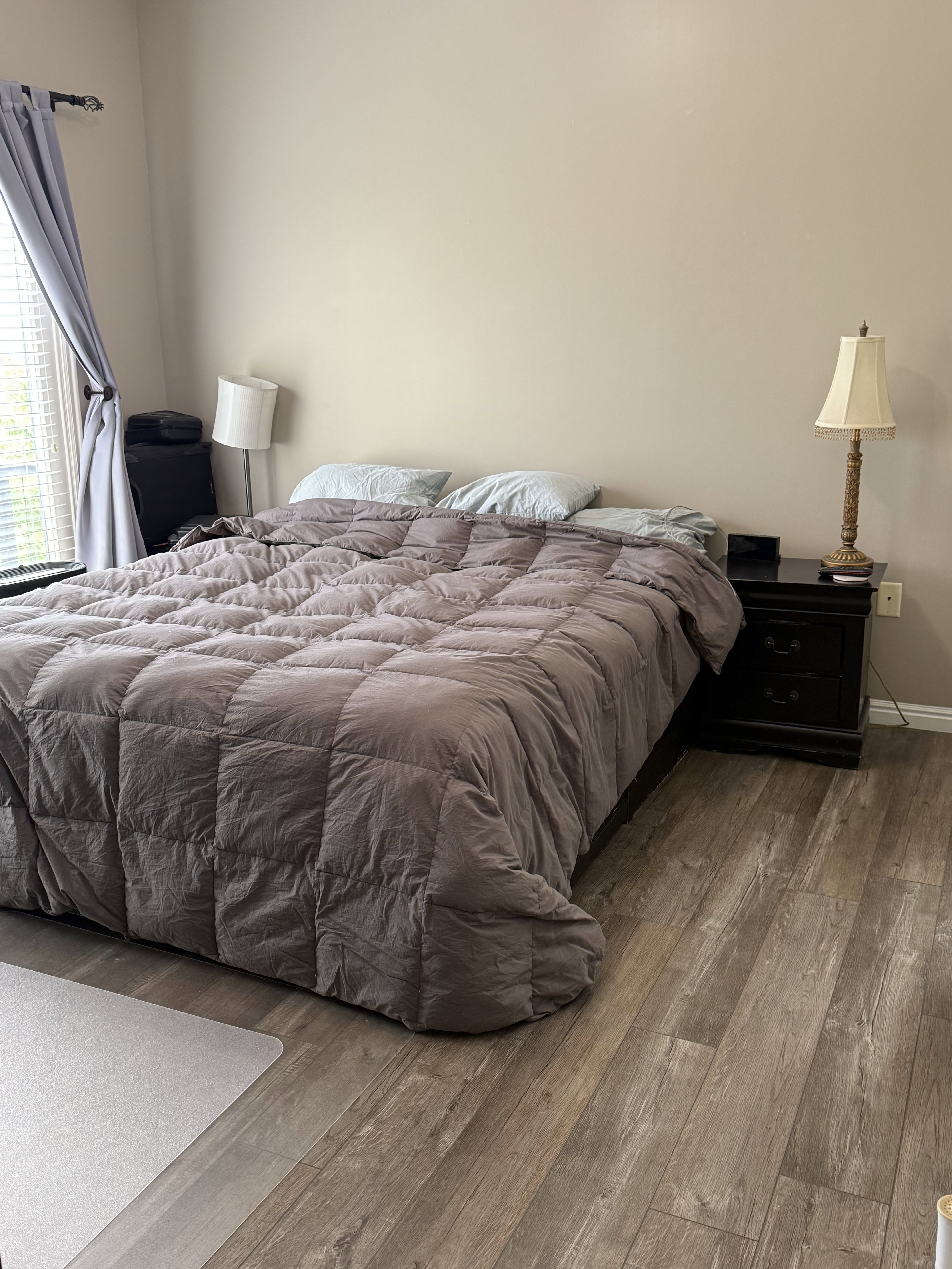 Spacious room featuring wood-finish flooring, neutral wall tones, and a large window with privacy blinds