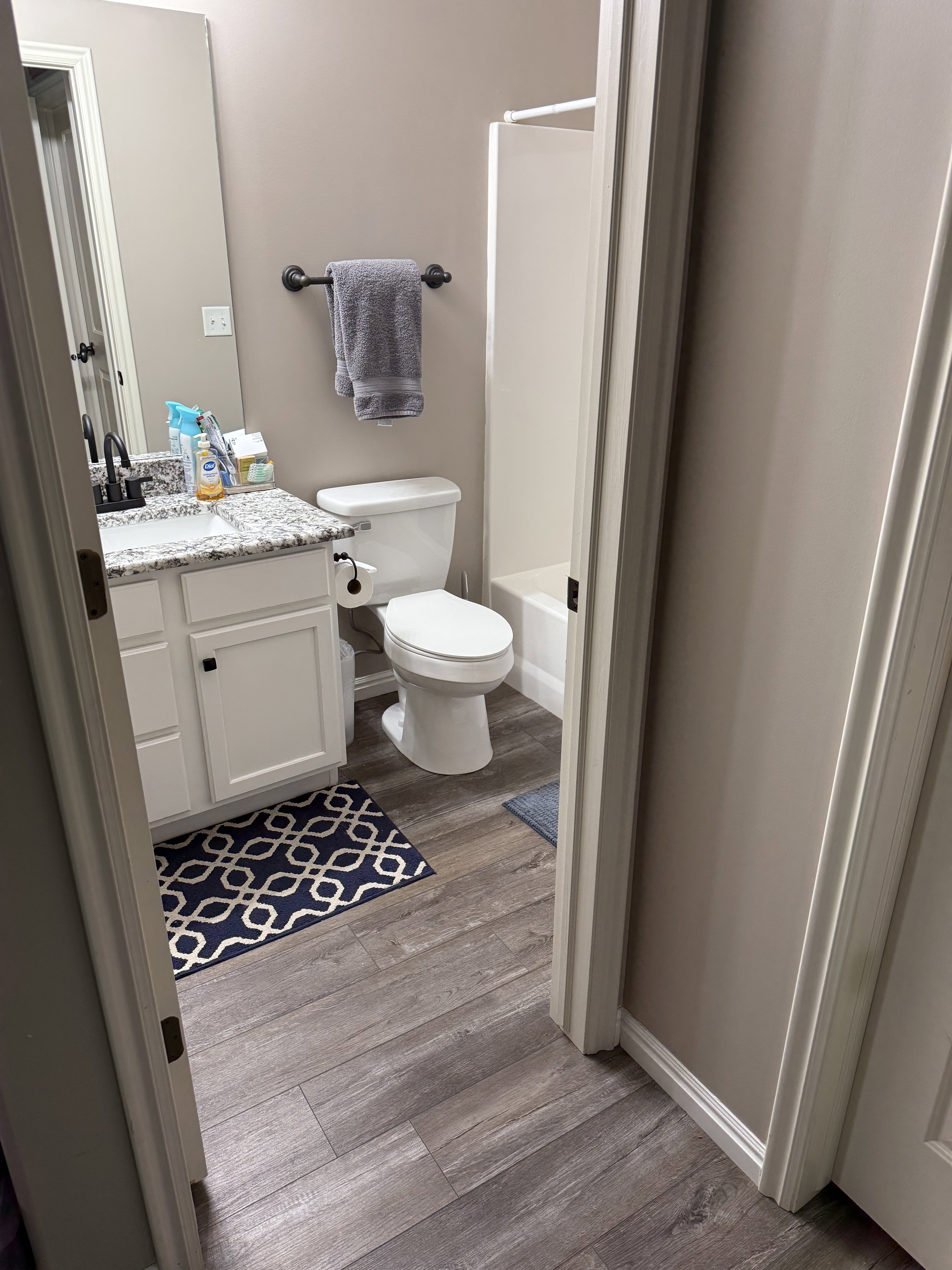 Bathroom featuring wood-finish flooring, a white vanity with granite-style countertop, an undermount sink with a black faucet, and a white shower-tub combination