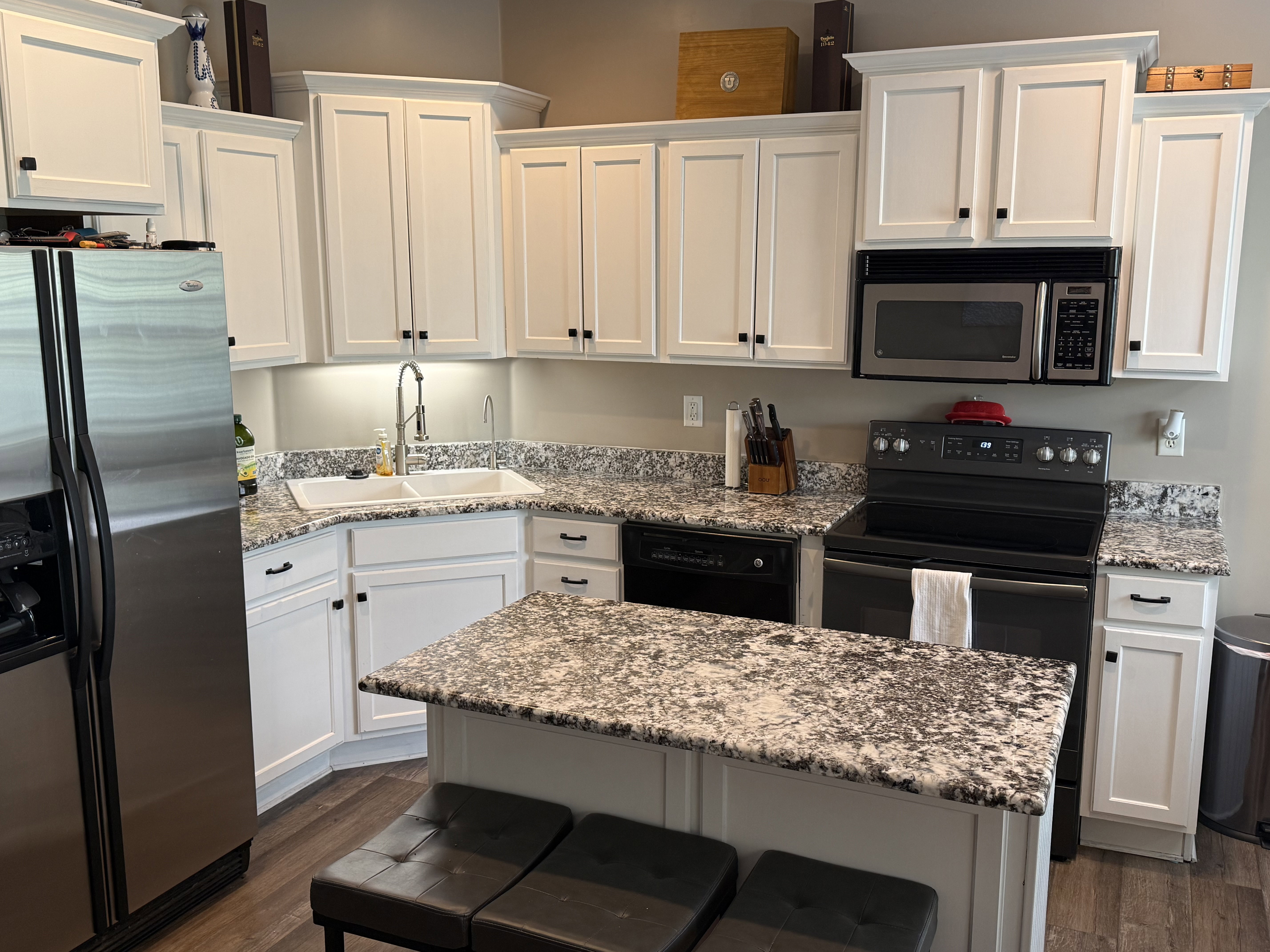 Modern kitchen featuring white shaker cabinetry, speckled countertops, stainless steel appliances, a corner sink, and wood-finish flooring