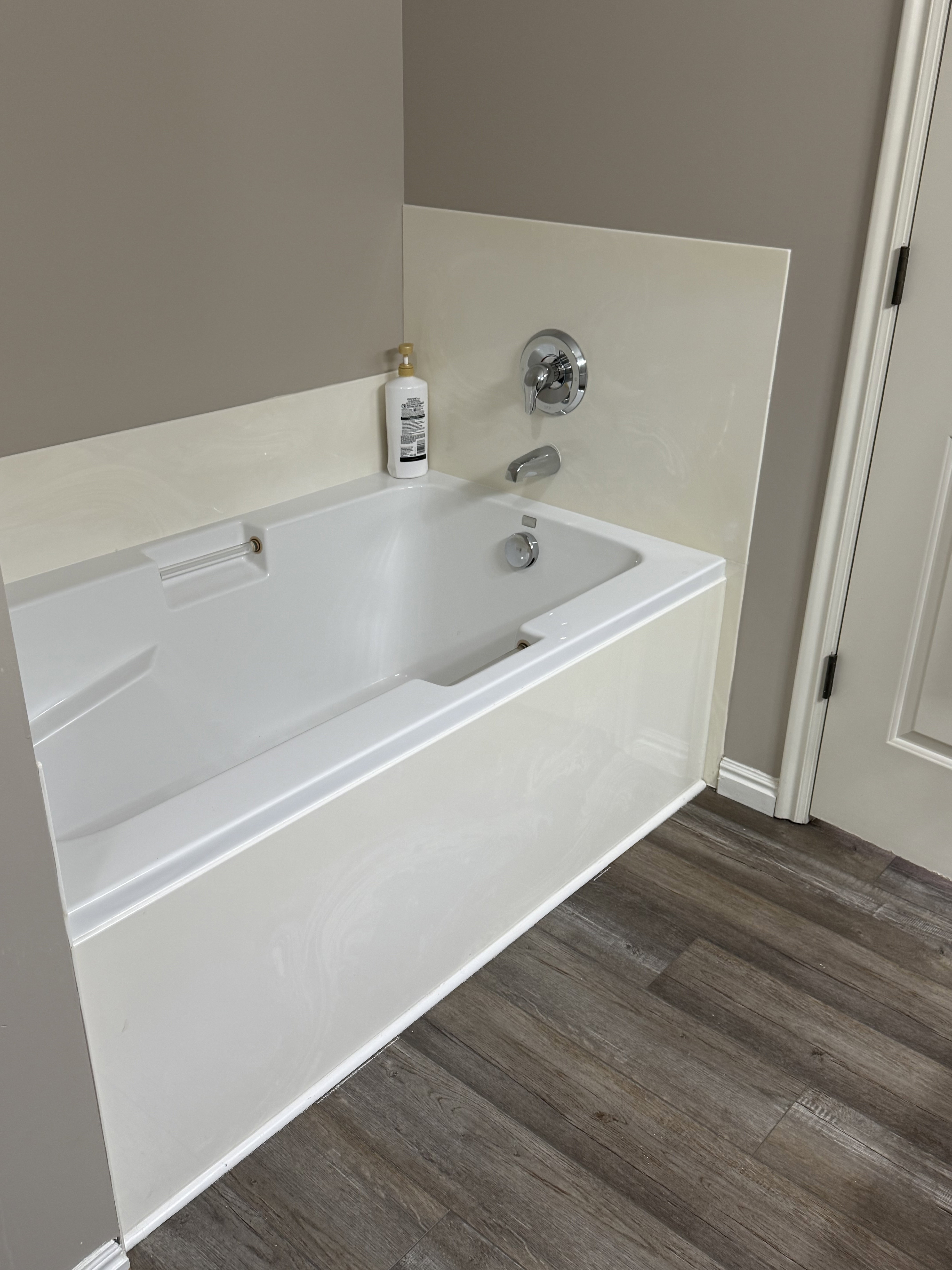 White bathtub with chrome fixtures, a cream-colored tile surround, and wood-finish flooring