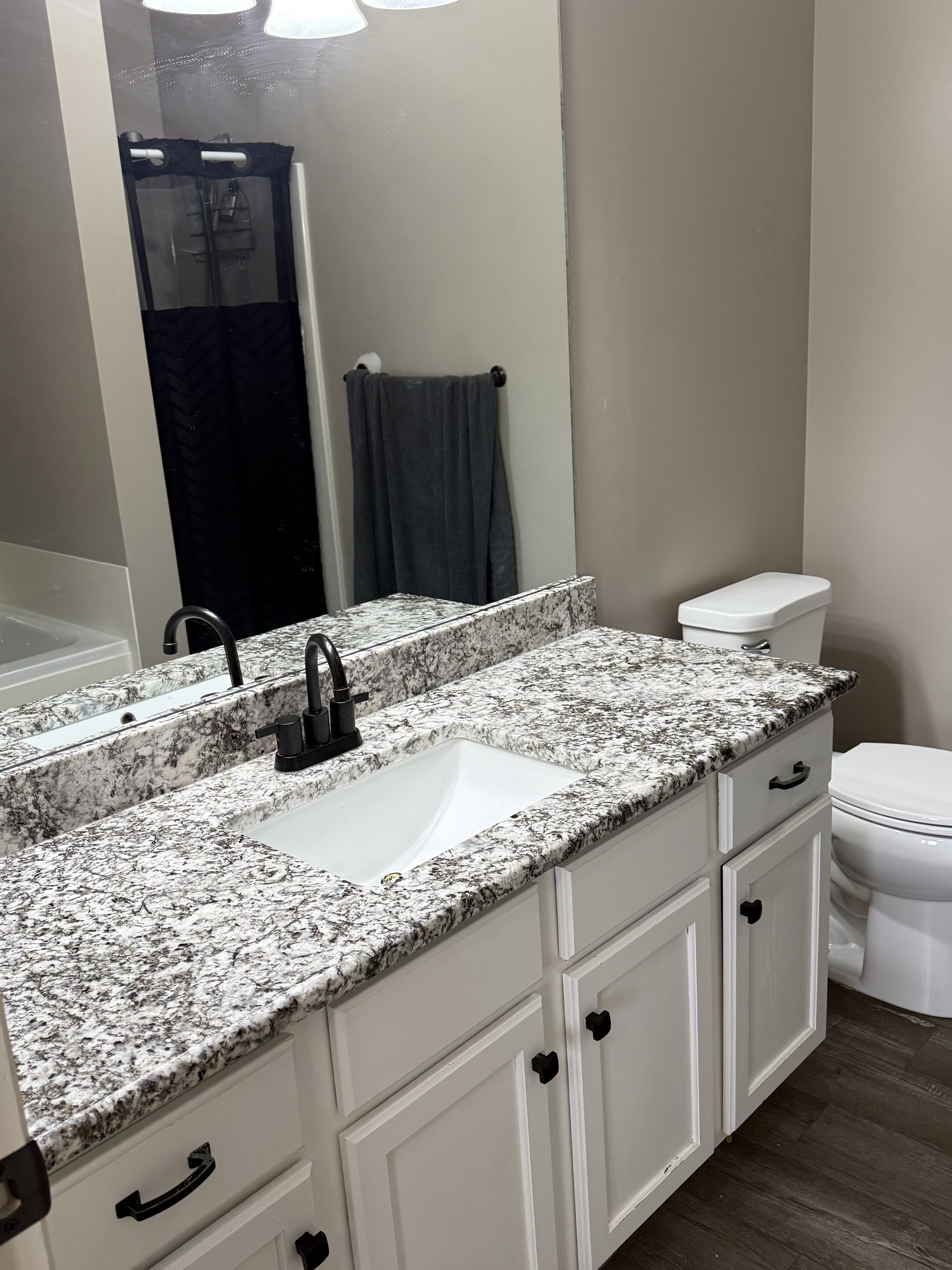 Bathroom vanity featuring a white rectangular undermount sink, granite-style countertop, and matte black faucet