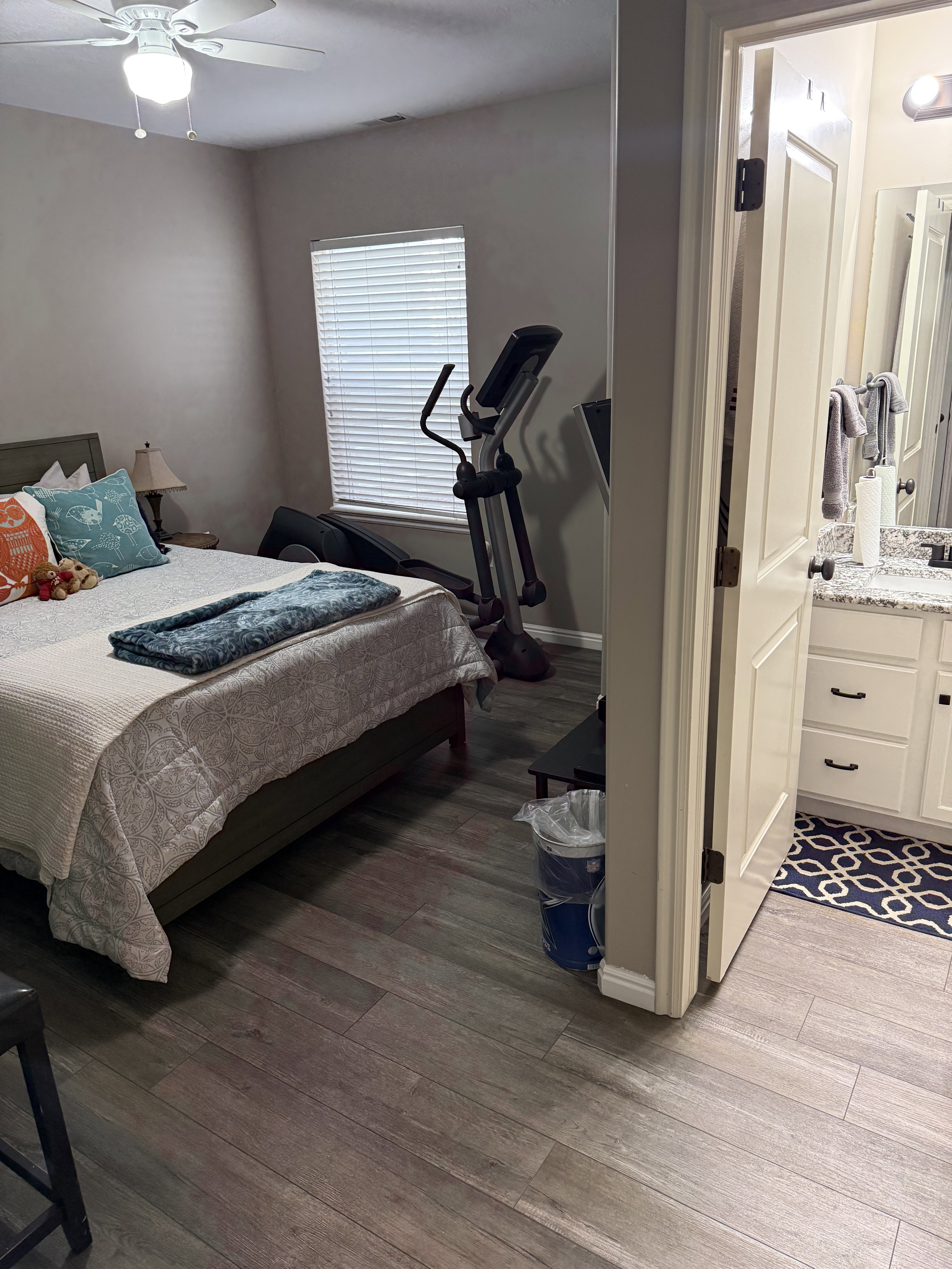 Bedroom featuring wood-finish plank flooring, ceiling fan with integrated lighting, and a window with blinds