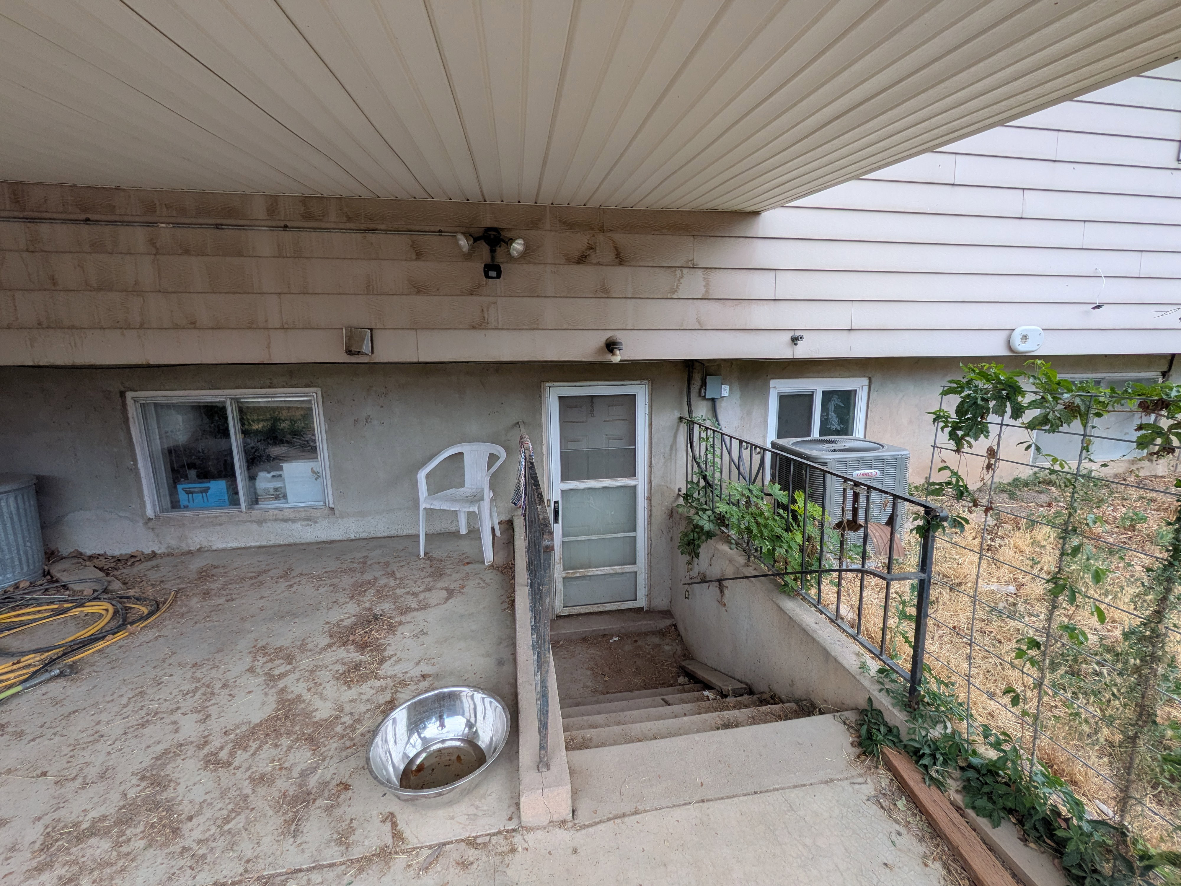 Lower-level exterior featuring a covered patio, concrete steps with metal railings, and dual-pane windows