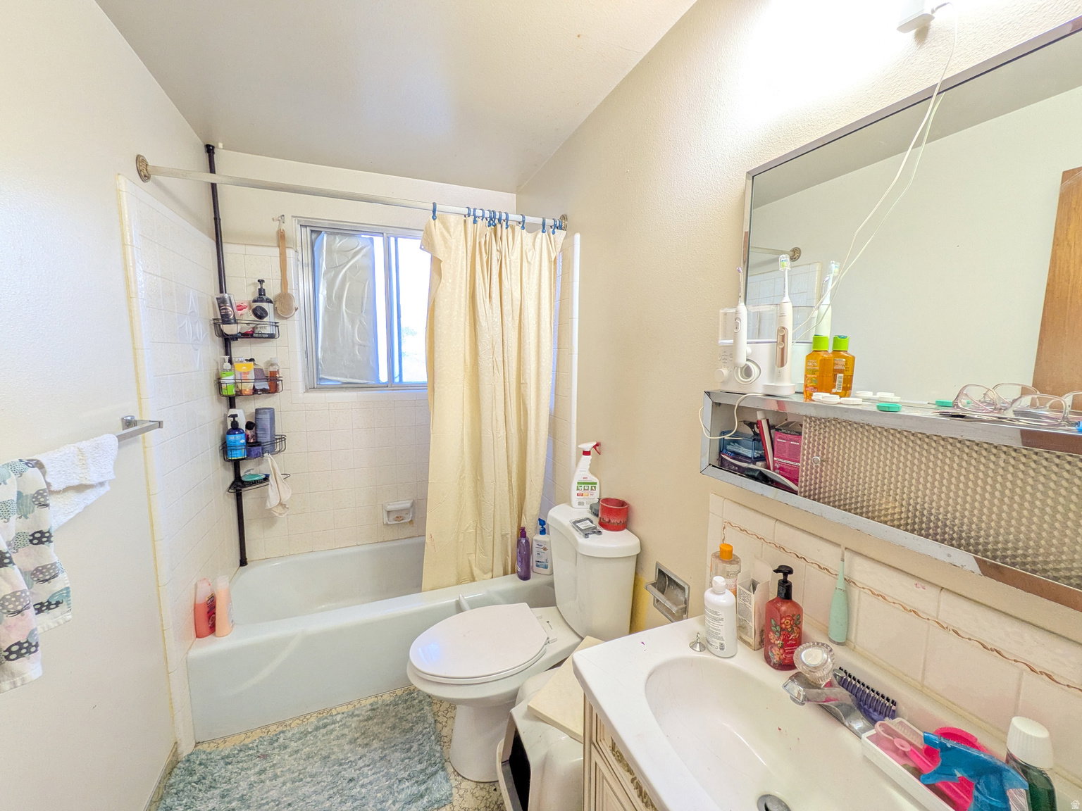 Bathroom featuring a combination bathtub and shower, a single vanity with an integrated sink, a toilet, and a framed mirror