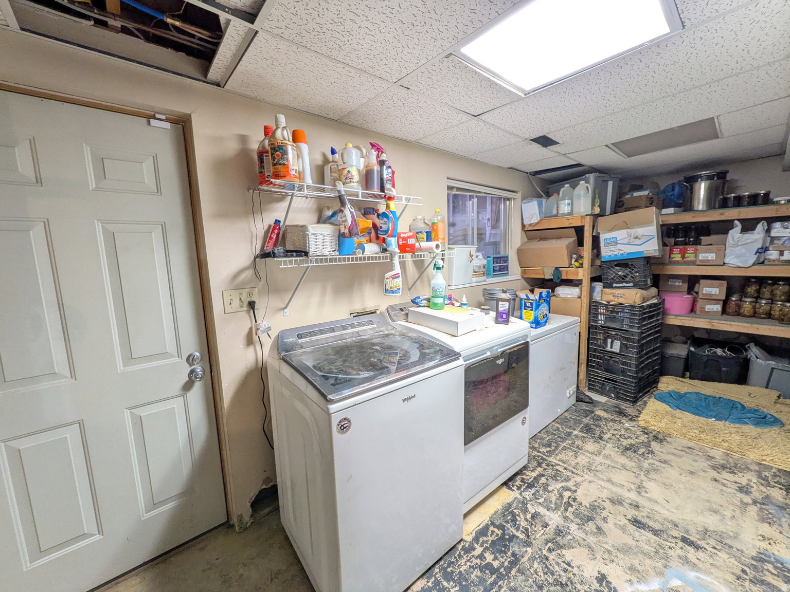 Utility room featuring a white paneled door, wall-mounted shelving, overhead fluorescent lighting, and a small window