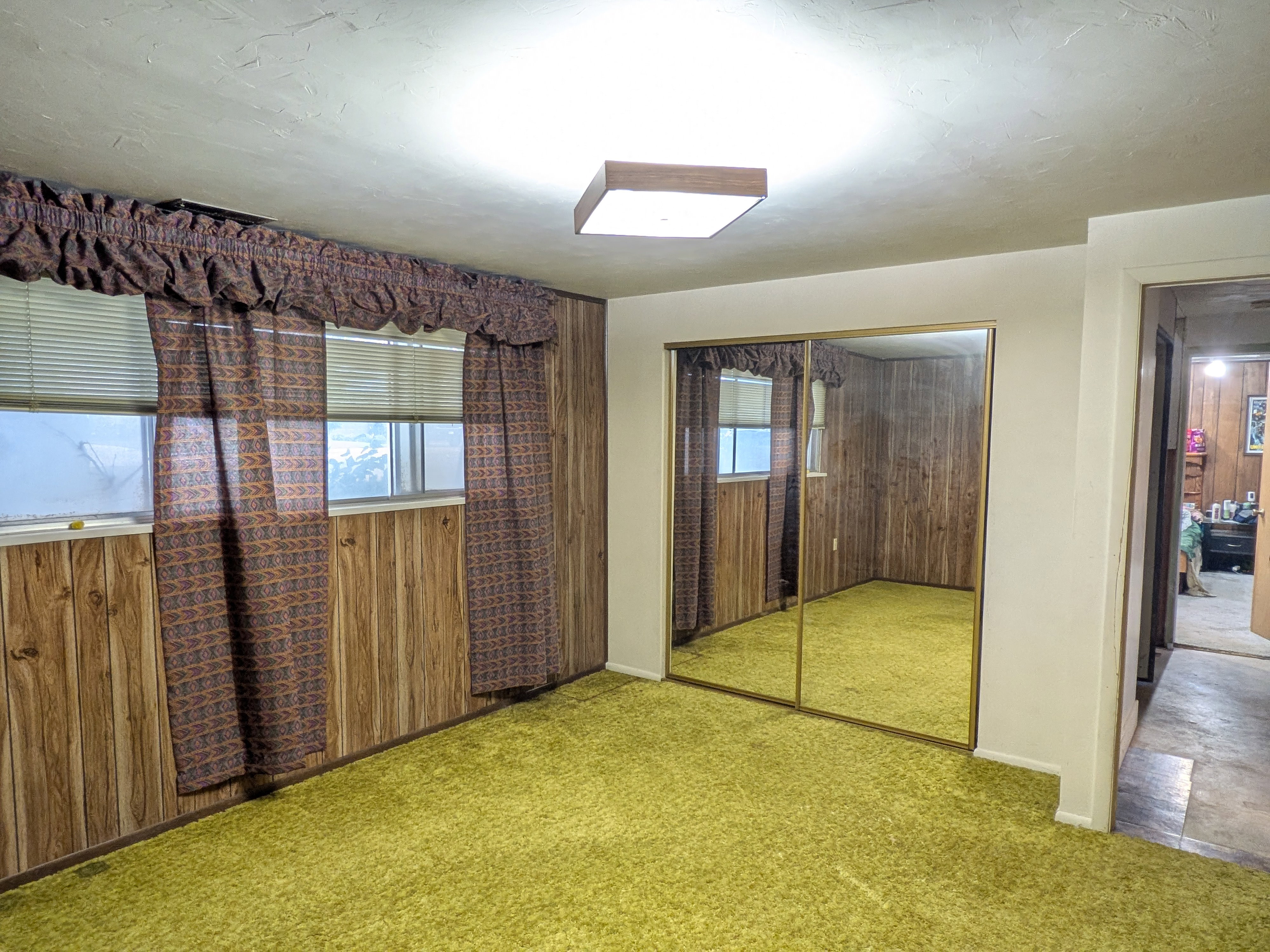 Room featuring wood-finish wall paneling, a large mirrored closet, and plush green carpeting