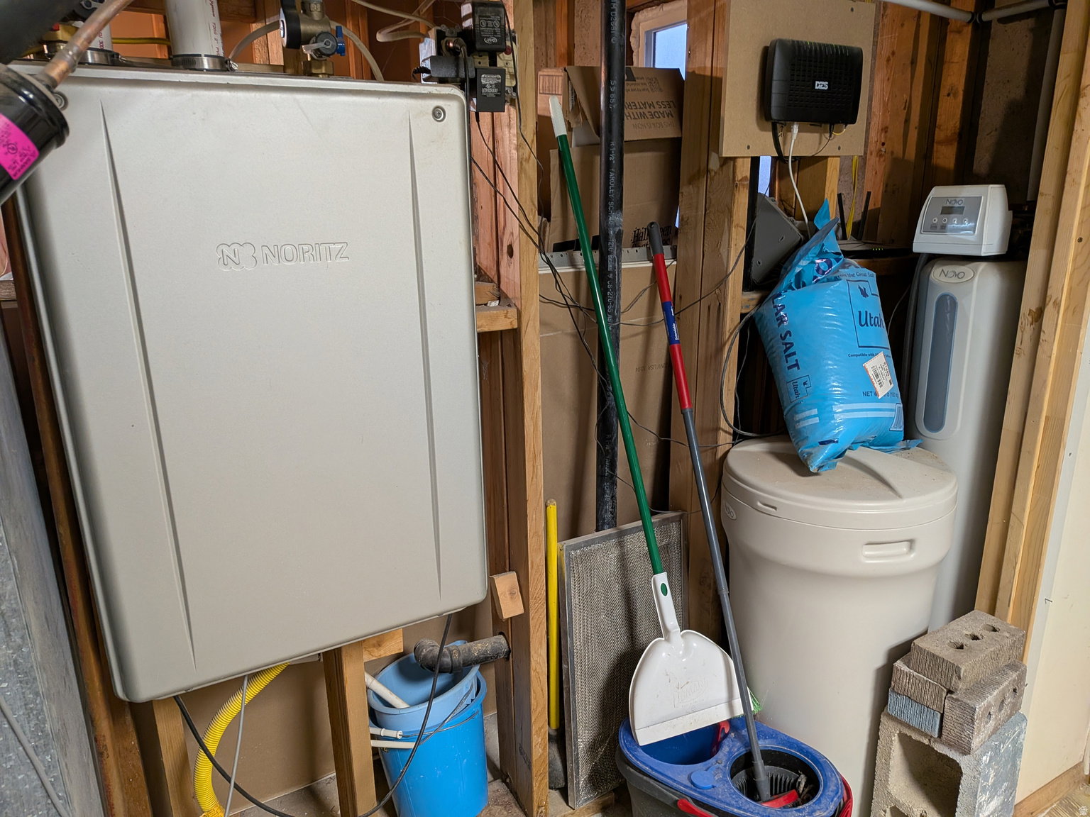 Noritz tankless water heater, water softener system, exposed wood framing, and utility connections