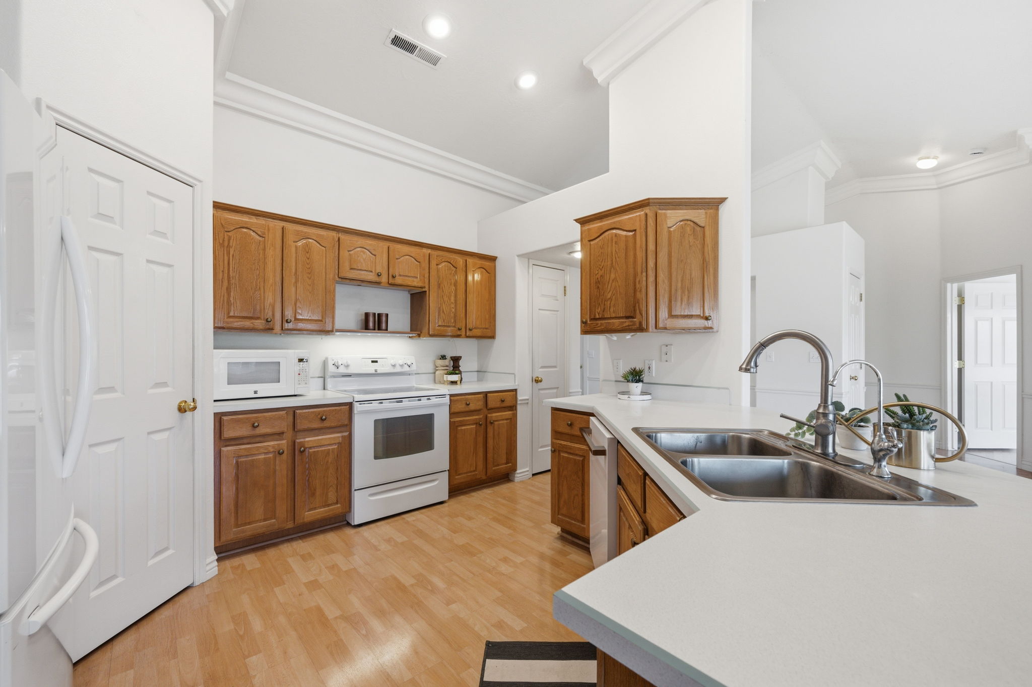 Kitchen featuring wood-finish flooring, light wood cabinetry, white countertops, and a double basin stainless steel sink with a high-arc faucet