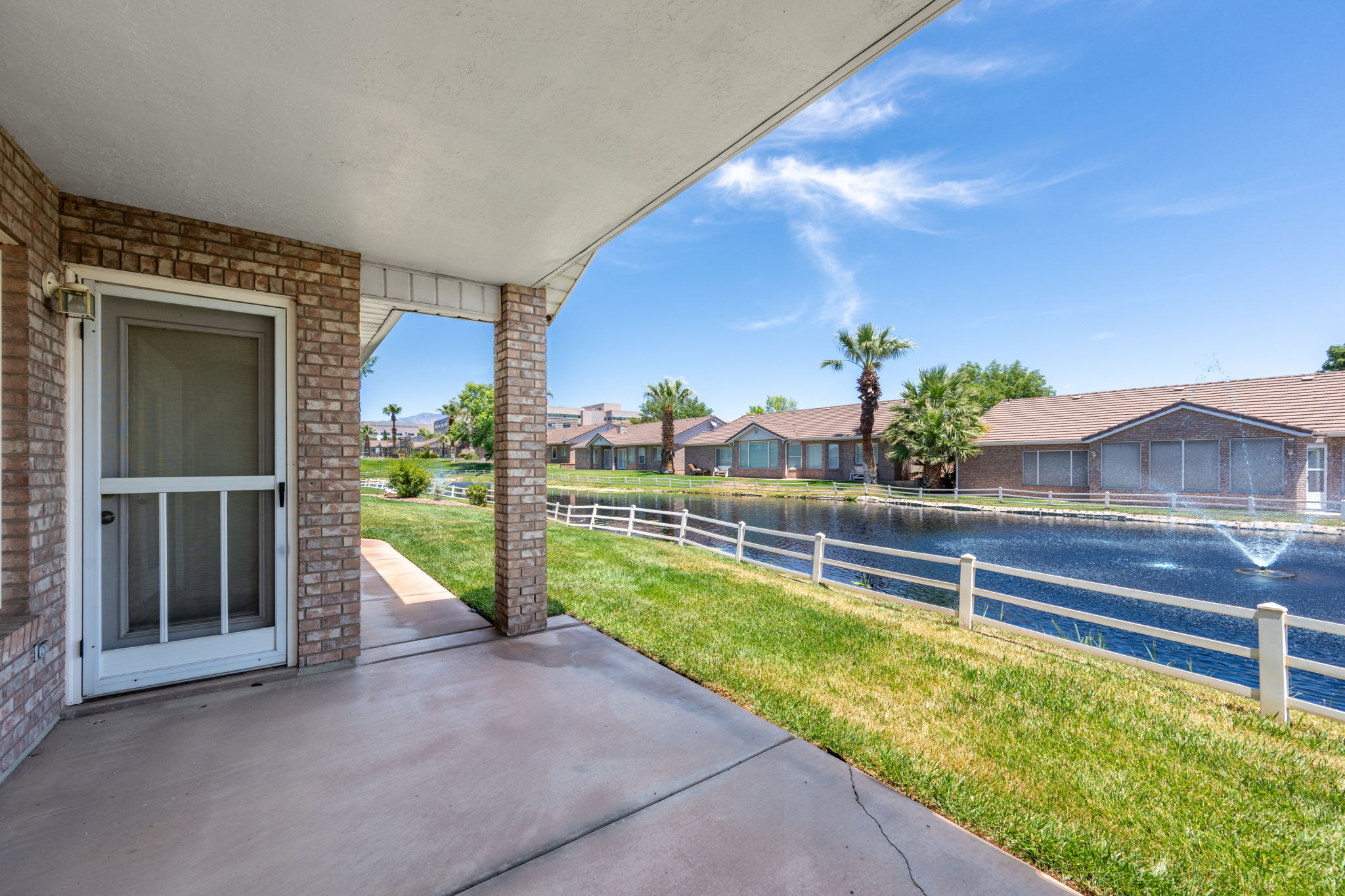 Covered patio with concrete flooring, brick columns, and a white screen door