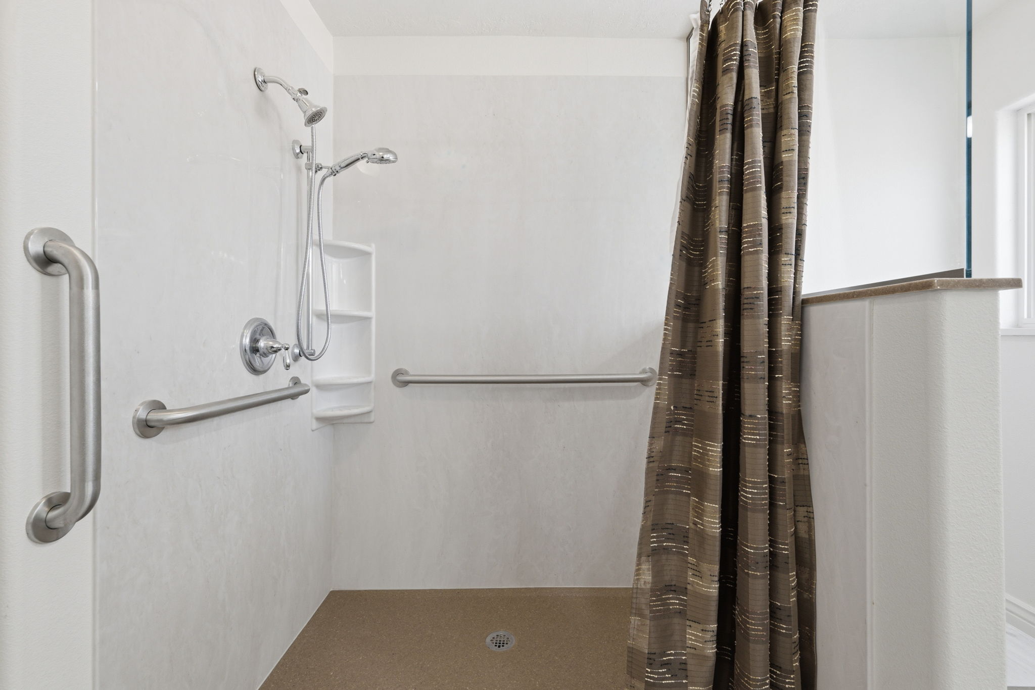 Walk-in shower with a neutral-toned floor, white paneling, and brushed nickel grab bars