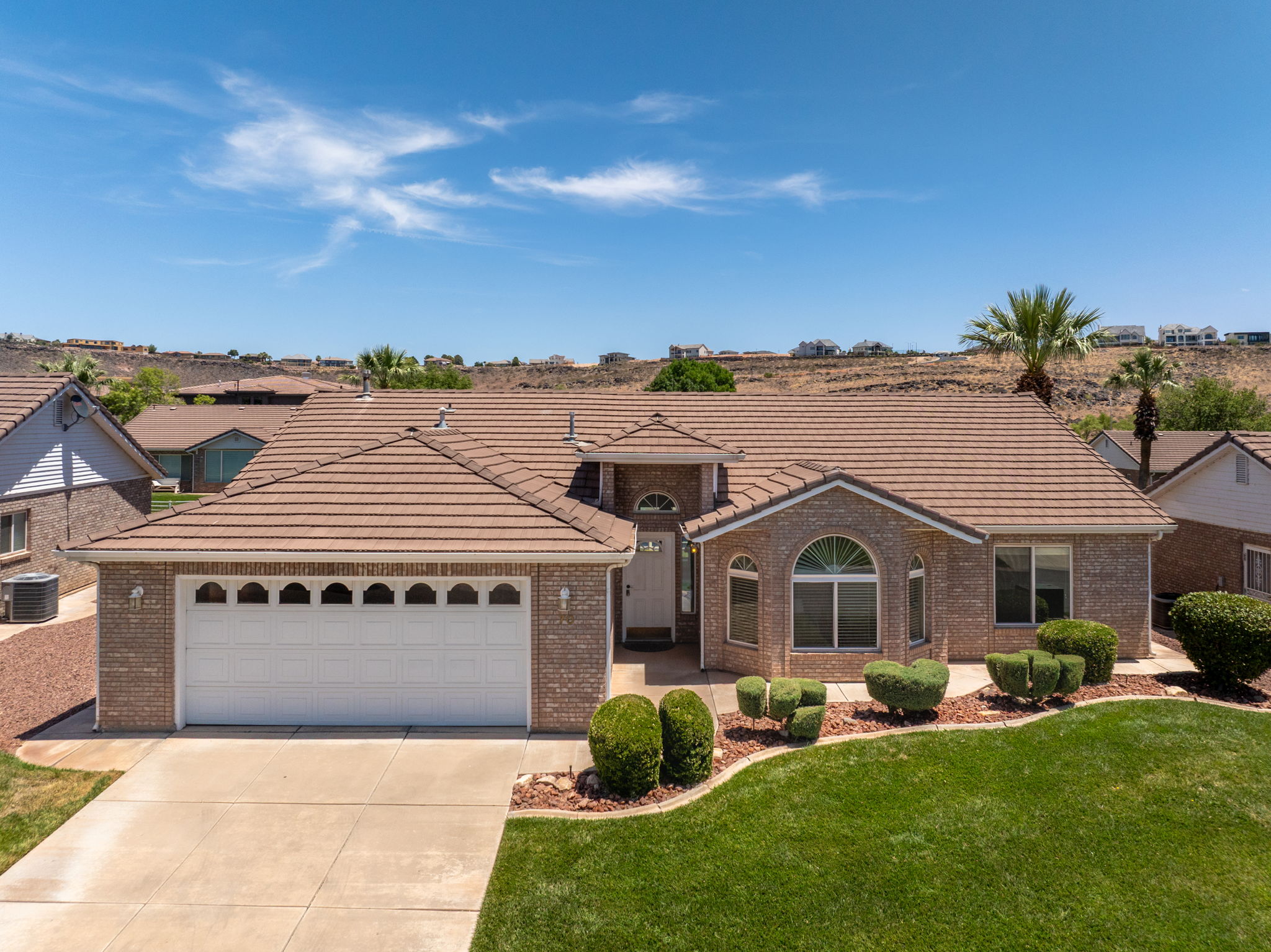 Brick exterior featuring a multi-gabled tile roof, an arched window, a two-car garage, and landscaped front yard with green lawn