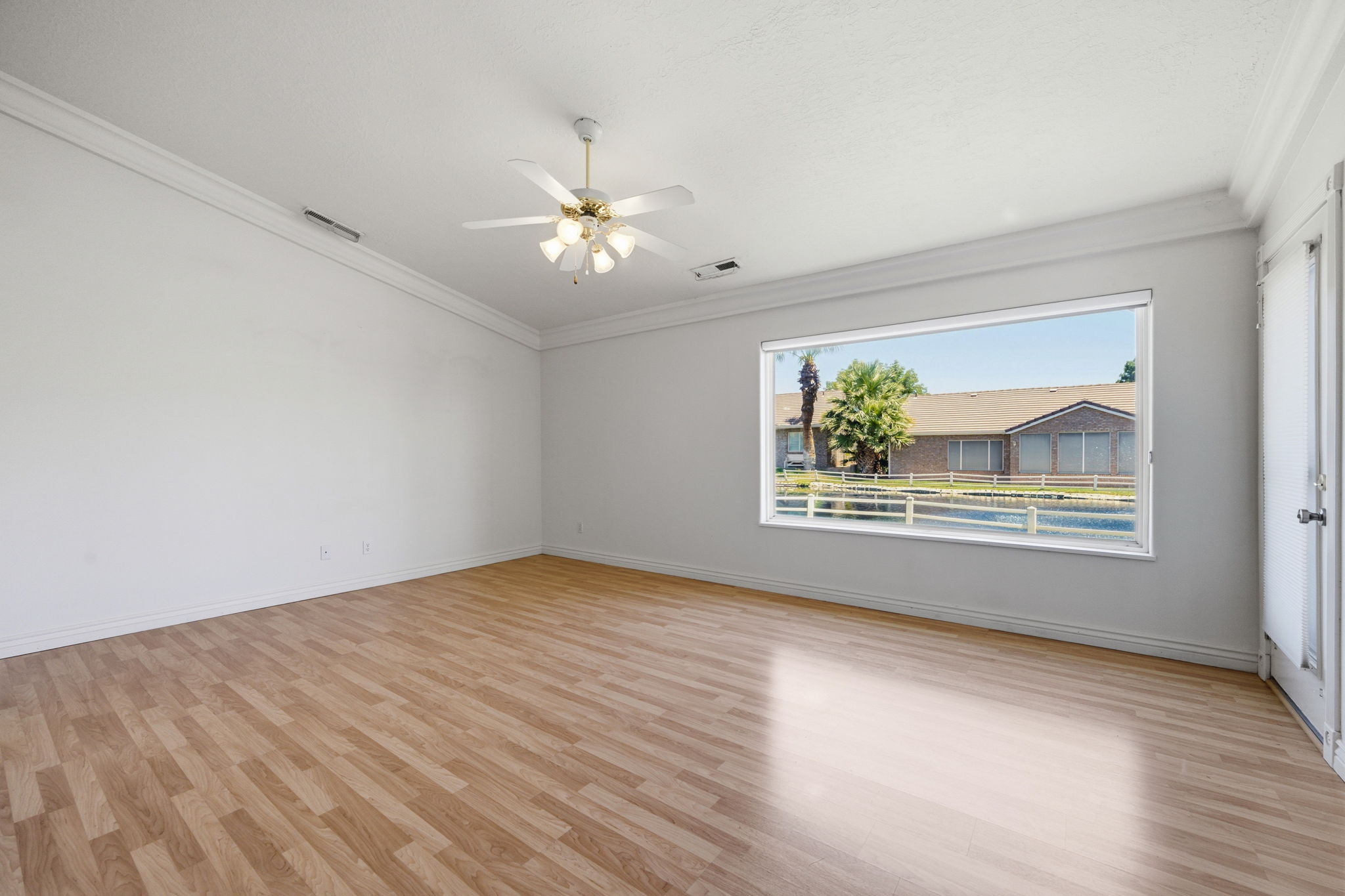 Spacious room featuring wood-finish flooring, white walls, and crown molding