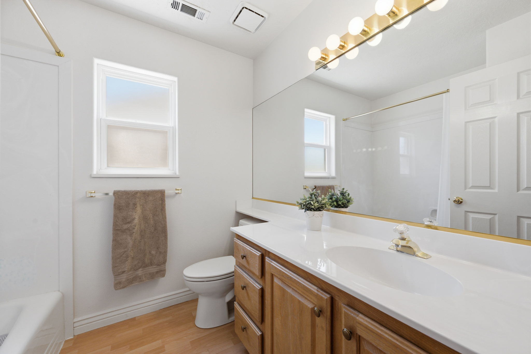 Bathroom featuring a wood-finish vanity with a white countertop and integrated sink, full-width mirror, and brass-tone vanity lighting